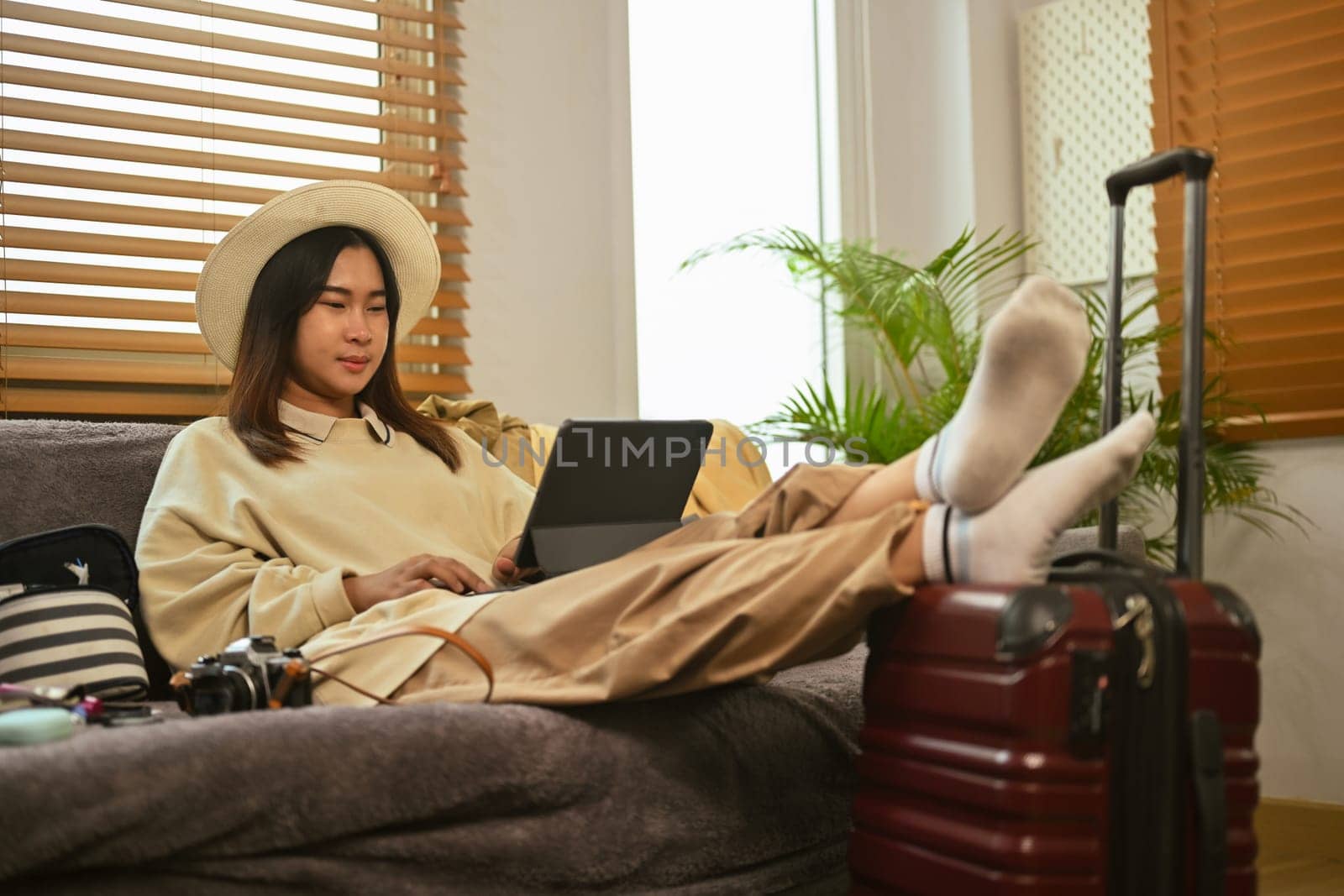 Relaxed young Asian woman making an online hotel reservation on digital tablet by prathanchorruangsak