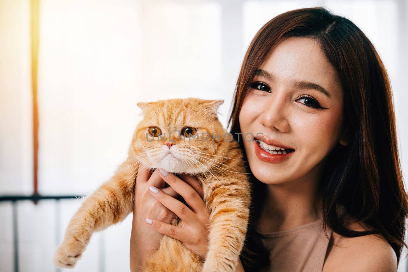 This close-up shot portrays a woman and her charming orange Scottish Fold cat, highlighting the warmth and companionship they enjoy in the comfort of their home. by Sorapop