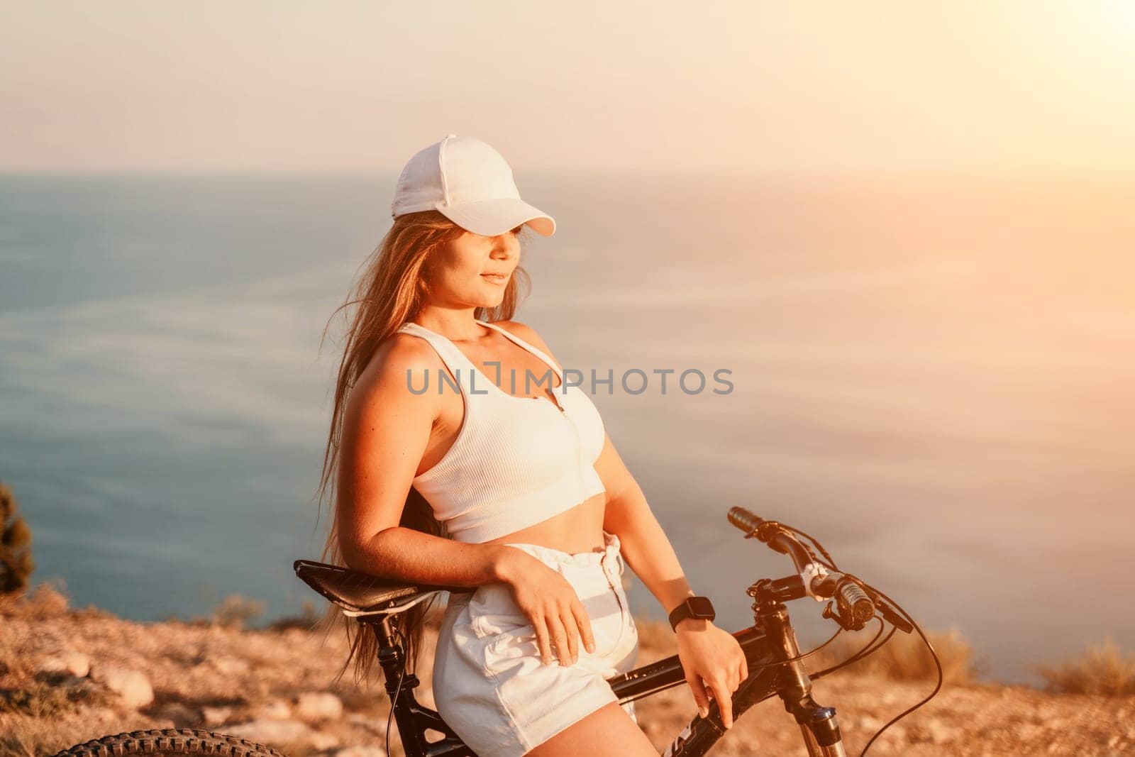 Woman travel bike sea. Happy woman cyclist sitting on her bike, enjoying the beautiful mountain and sea landscape, signifying the idea of an adventurous bike ride