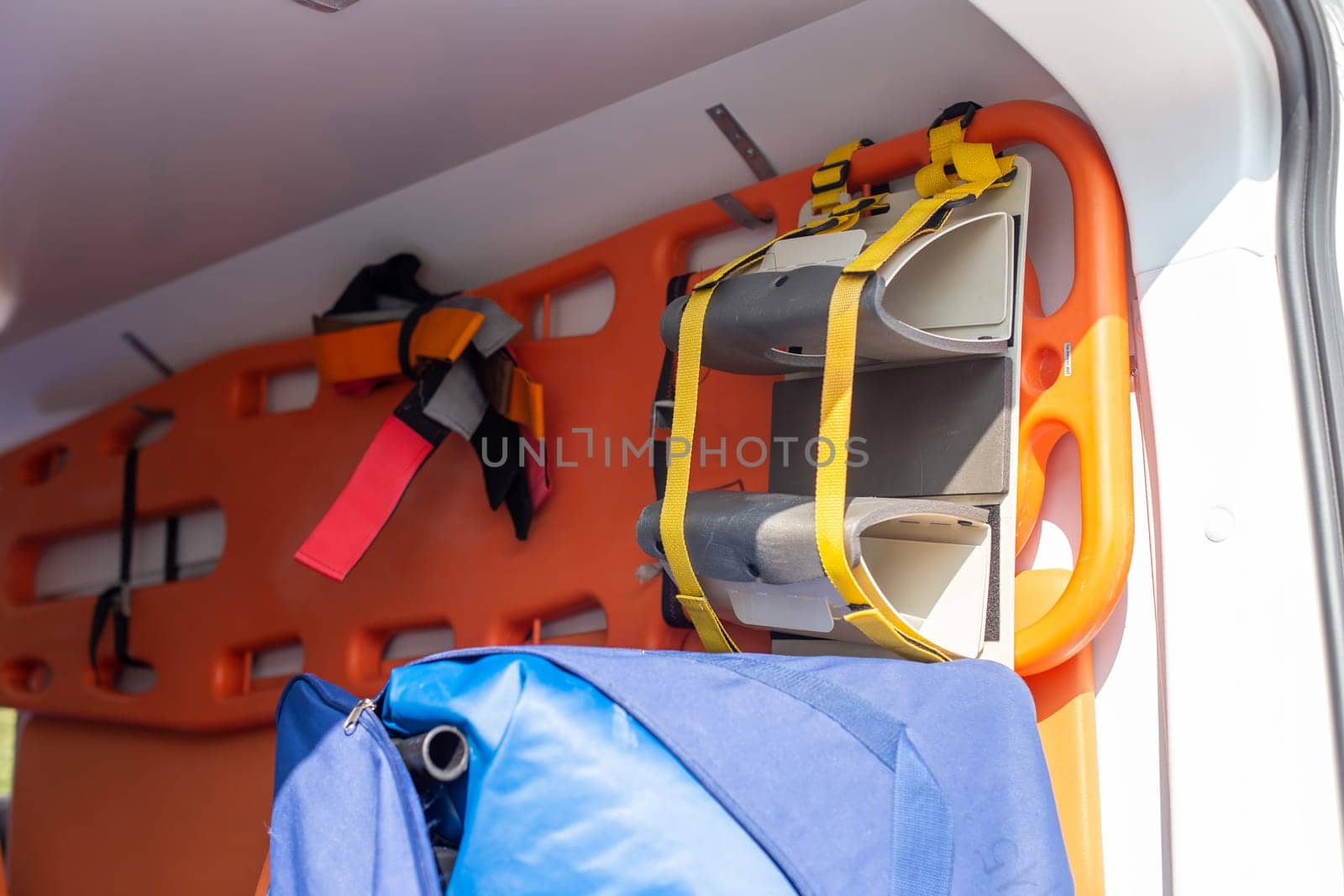 A close-up of an orange stretcher with a fixation hanging on the wall in the cabin of an ambulance.