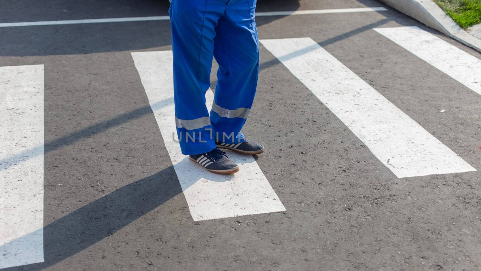 Partial view of a paramedic in blue uniform standing on a zebra crossing, focus on feet