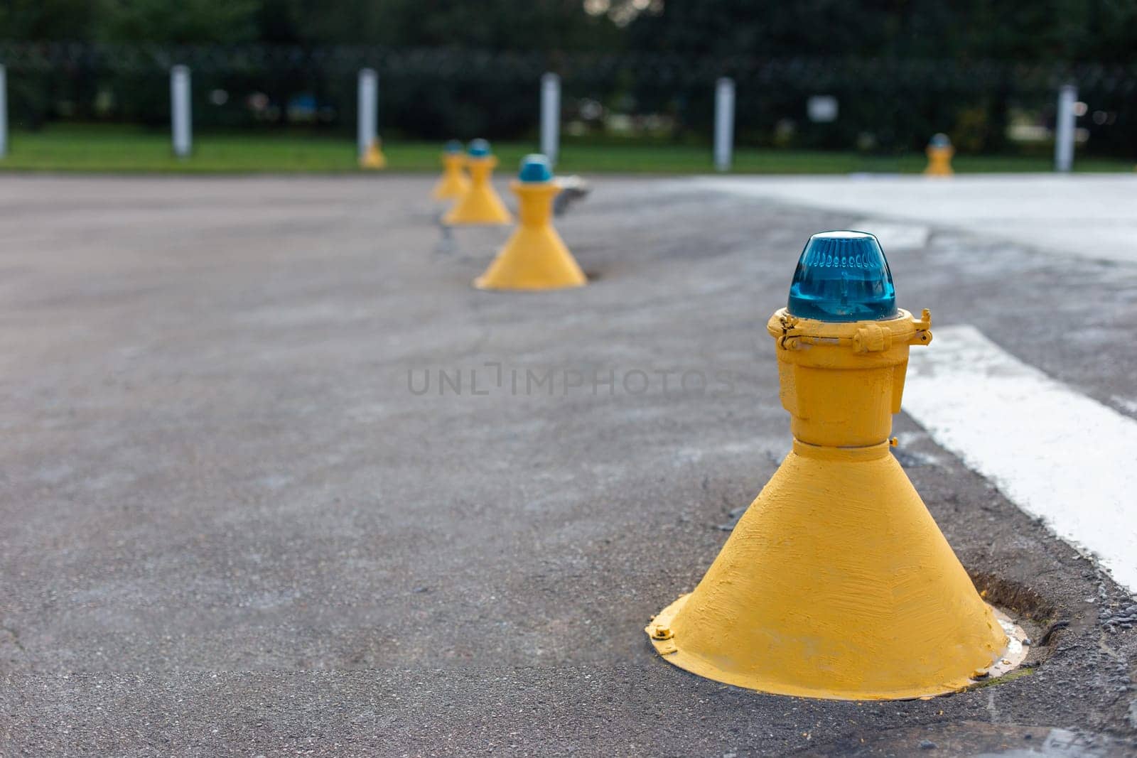 Row of yellow airfield ground lights with blue tops, used for runway and taxiway guidance at an airport by Zakharova