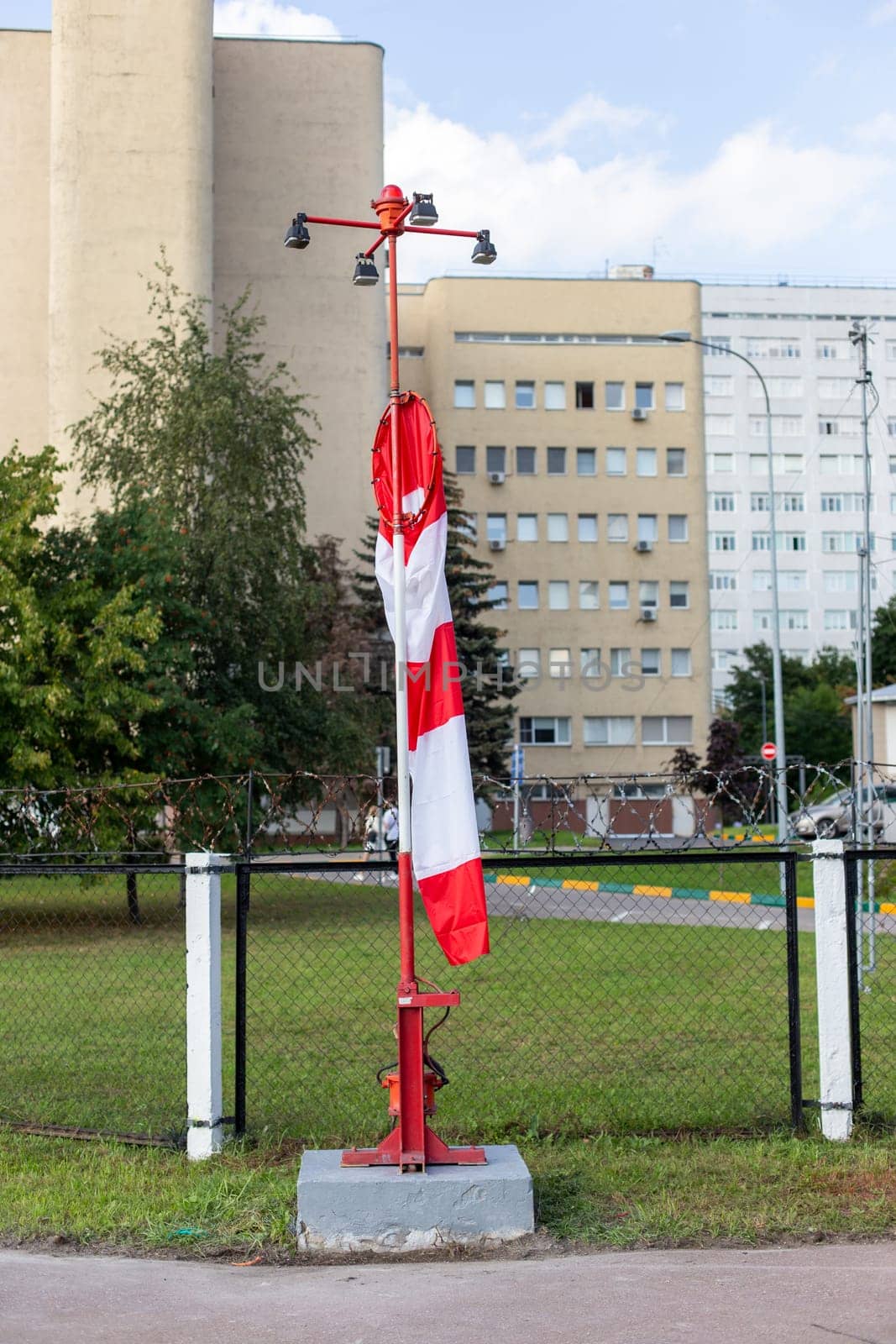 Moscow, Moscow region, Russia - 03.09.2023:A striped wind direction indicator wrapped around its pole on the airfield with buildings in the background by Zakharova