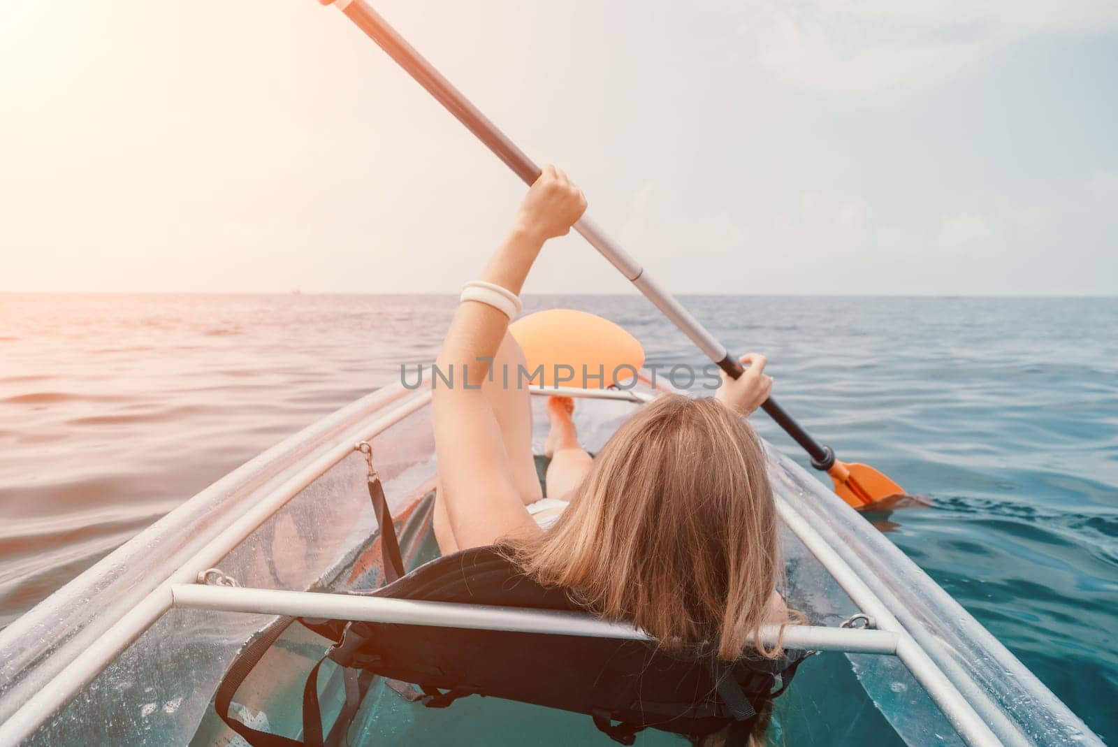 Woman in kayak back view. Happy young woman with long hair floating in transparent kayak on the crystal clear sea. Summer holiday vacation and cheerful female people having fun on the boat.