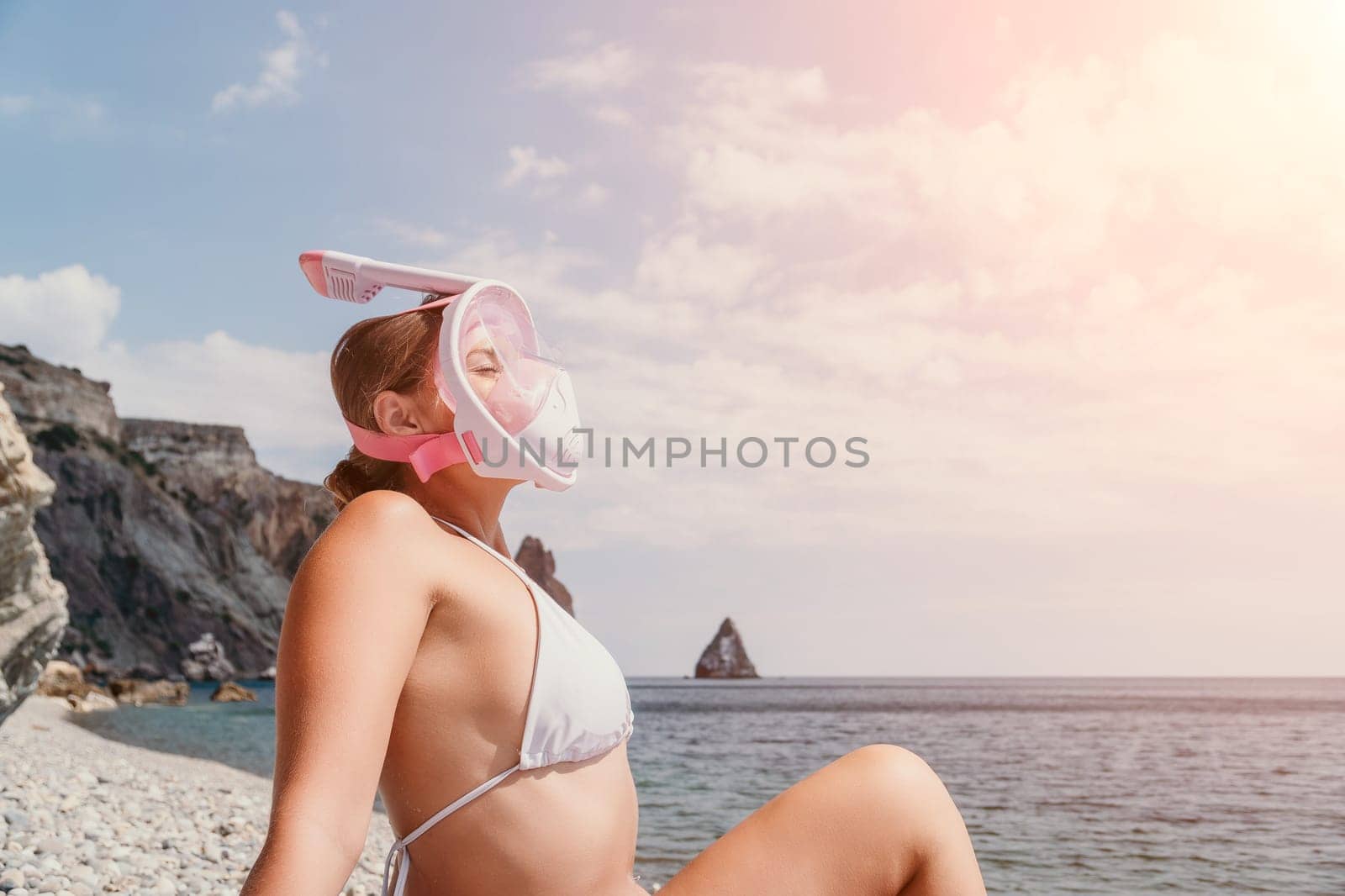 Young happy woman in white bikini and wearing pink mask gets ready for sea snorkeling. Positive smiling woman relaxing and enjoying water activities with family summer travel holidays vacation on sea. by panophotograph