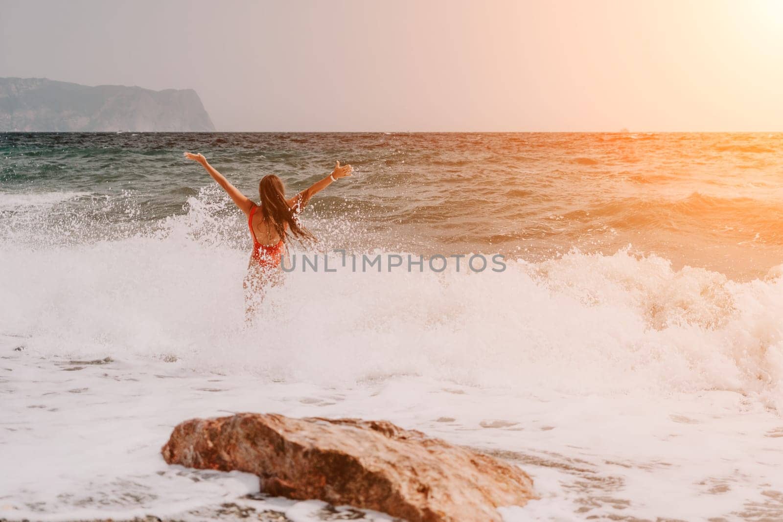 Woman summer travel sea. Happy tourist in red bikini enjoy taking picture outdoors for memories. Woman traveler posing on beach at sea surrounded by volcanic mountains, sharing travel adventure joy by panophotograph