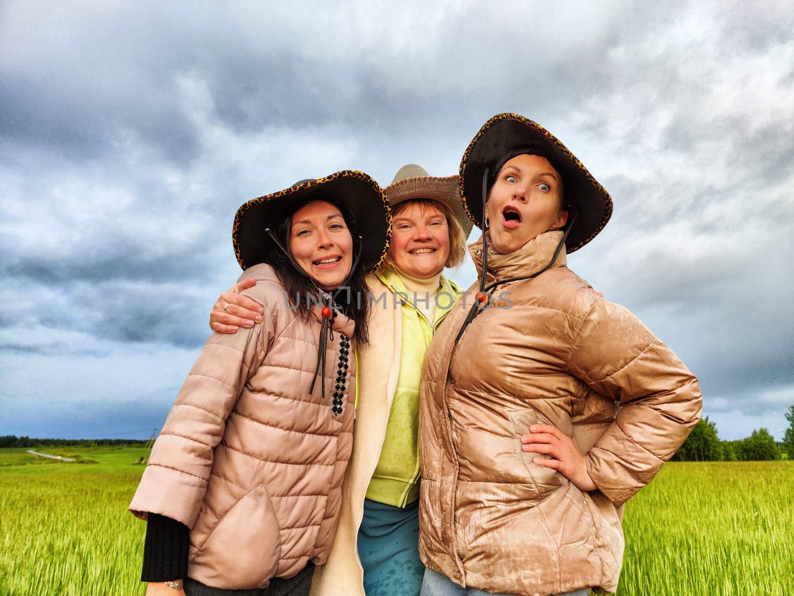 Adult girls looking like a cowboys in hats in a field and with a stormy sky with clouds posing in the rain. Women having fun outdoors on rural and rustic nature