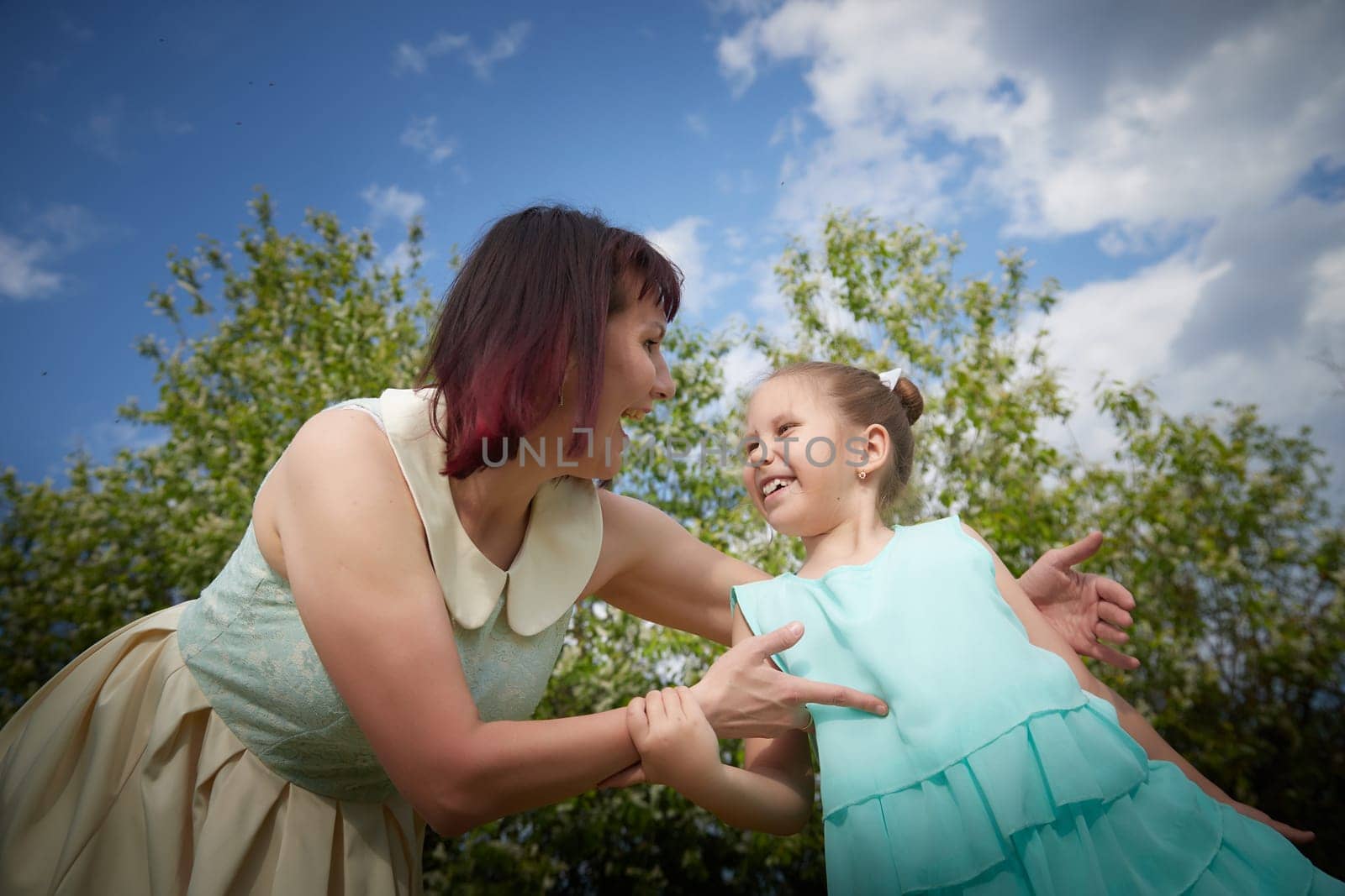 Happy mother and daughter enjoying rest, playing and fun on nature on a green lawn and with blooming apple tree in the background. Woman and girl resting outdoors in summer and spring day