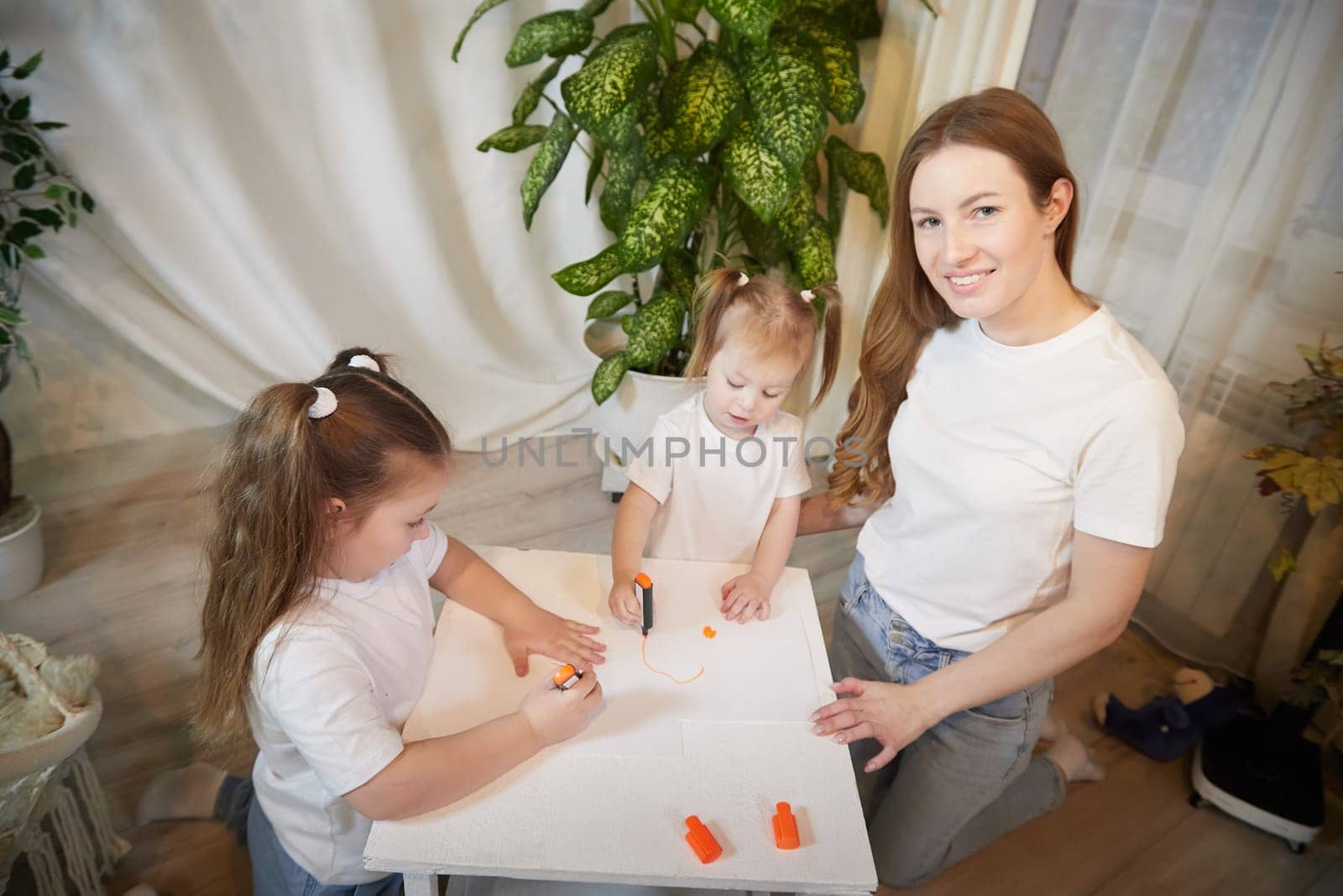 Young mother or babysitter, little daughter, sister teenager girl drawing at table in room. Painting, doing homework. Family enjoying leisure at home