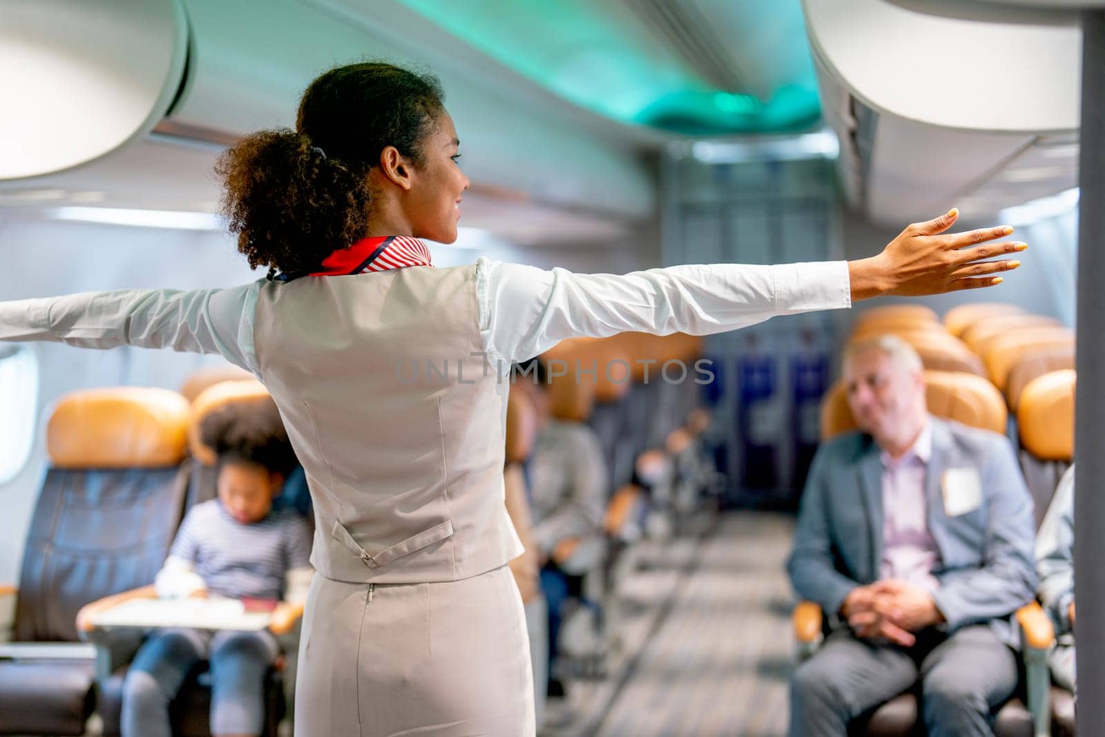 Air hostess or airline staff woman demostrate and guide the emergency exit of airplane to the passenger before take of the flight to the other city. by nrradmin