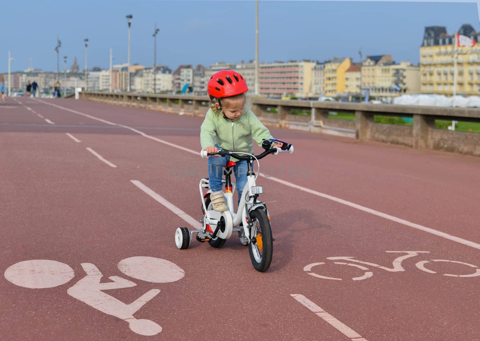 3 Years old Girl in helmet learns riding a four-wheeled bicycle