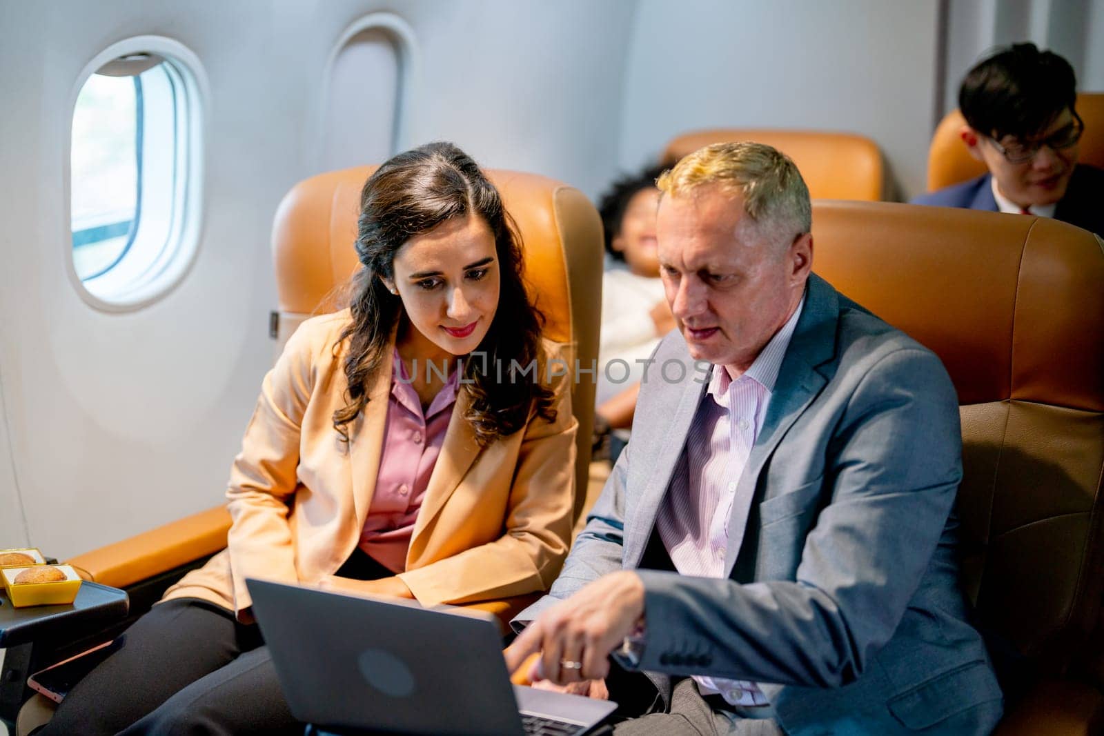 Caucasian business senior man and young woman discuss about work together using laptop during sit in airplane of flight to the other city.