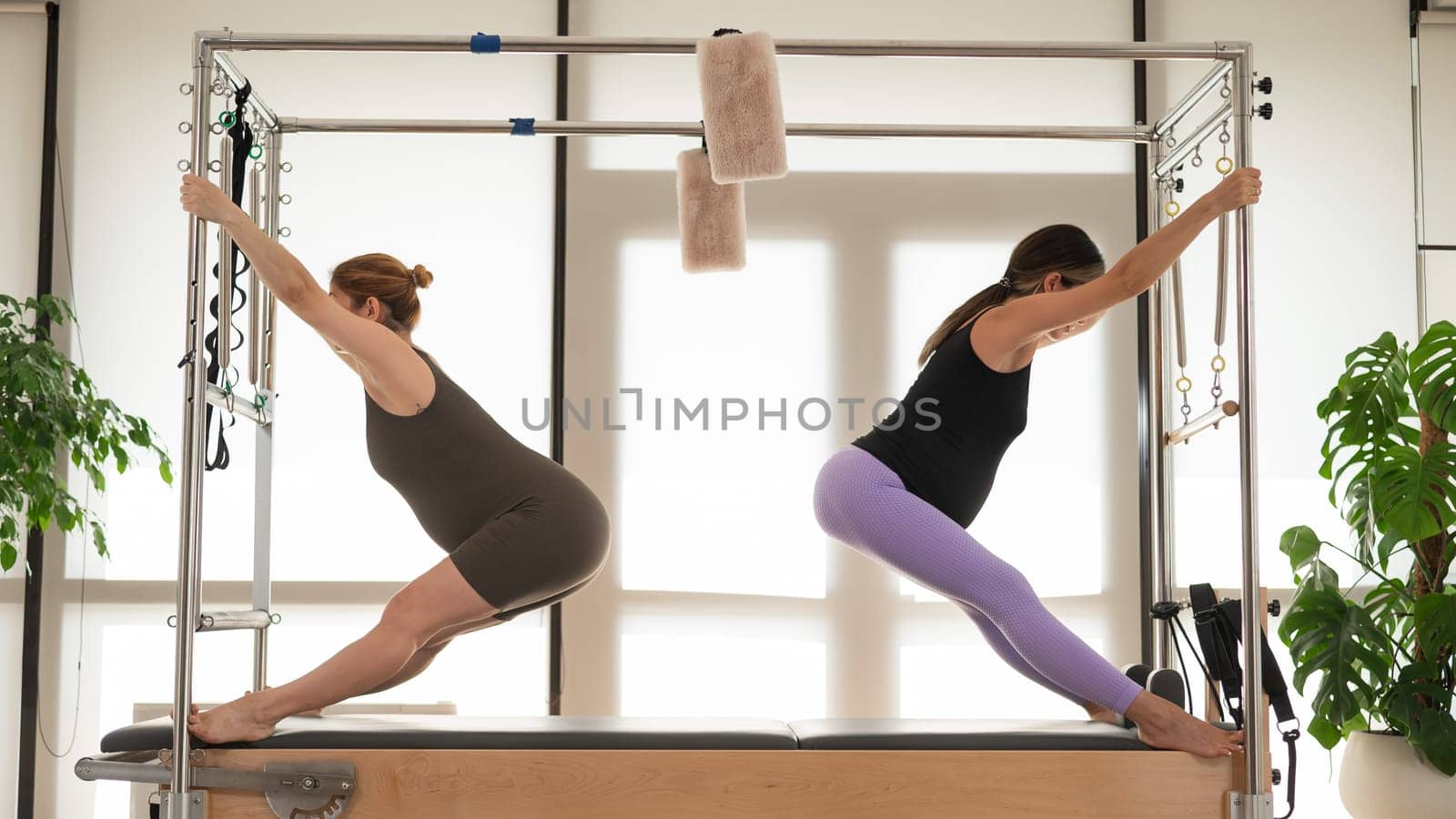 Two pregnant women are doing Pilates on a Cadillac reformer