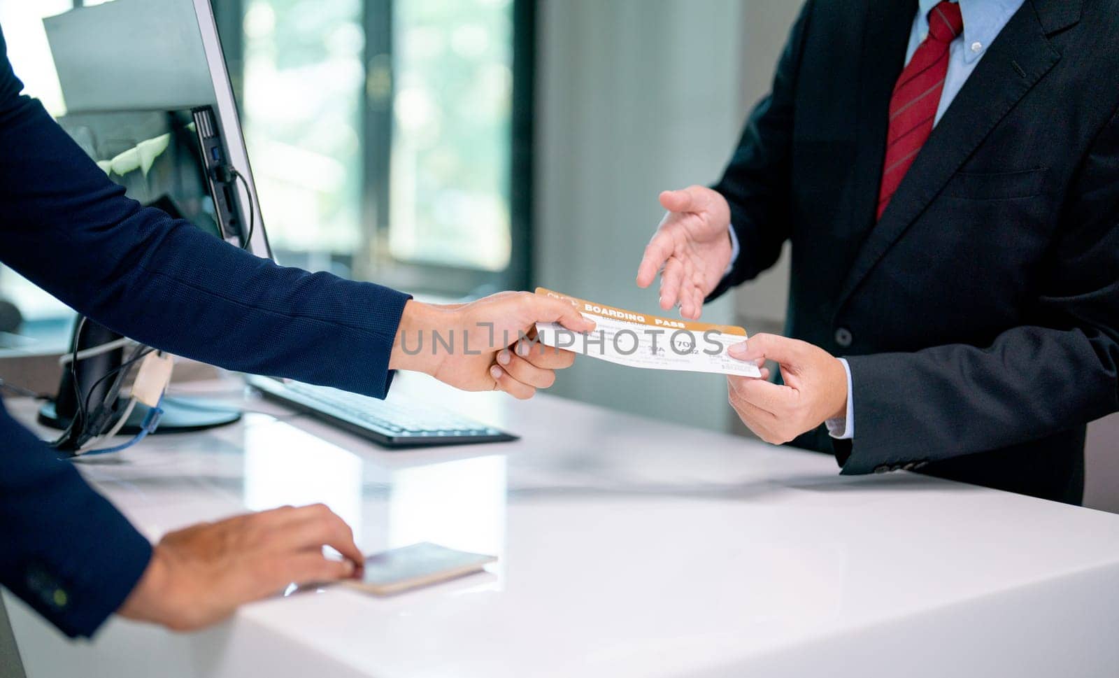 Close up hands of airline staff give boarding pass for flight to the customer at service counter in the airport.