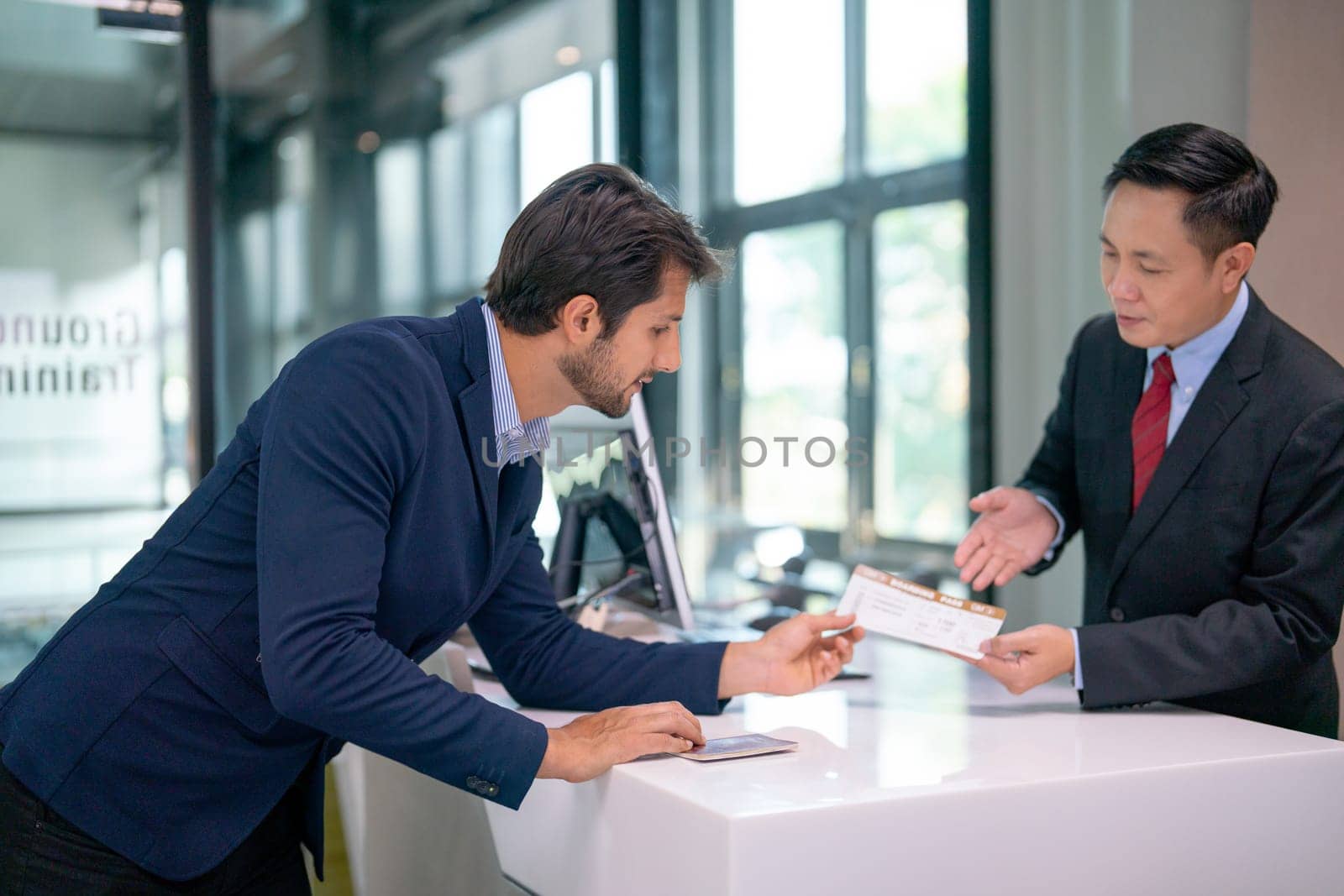 Airline staff give boarding pass to the passenger business man and explain about the detail at counter service in the airport.