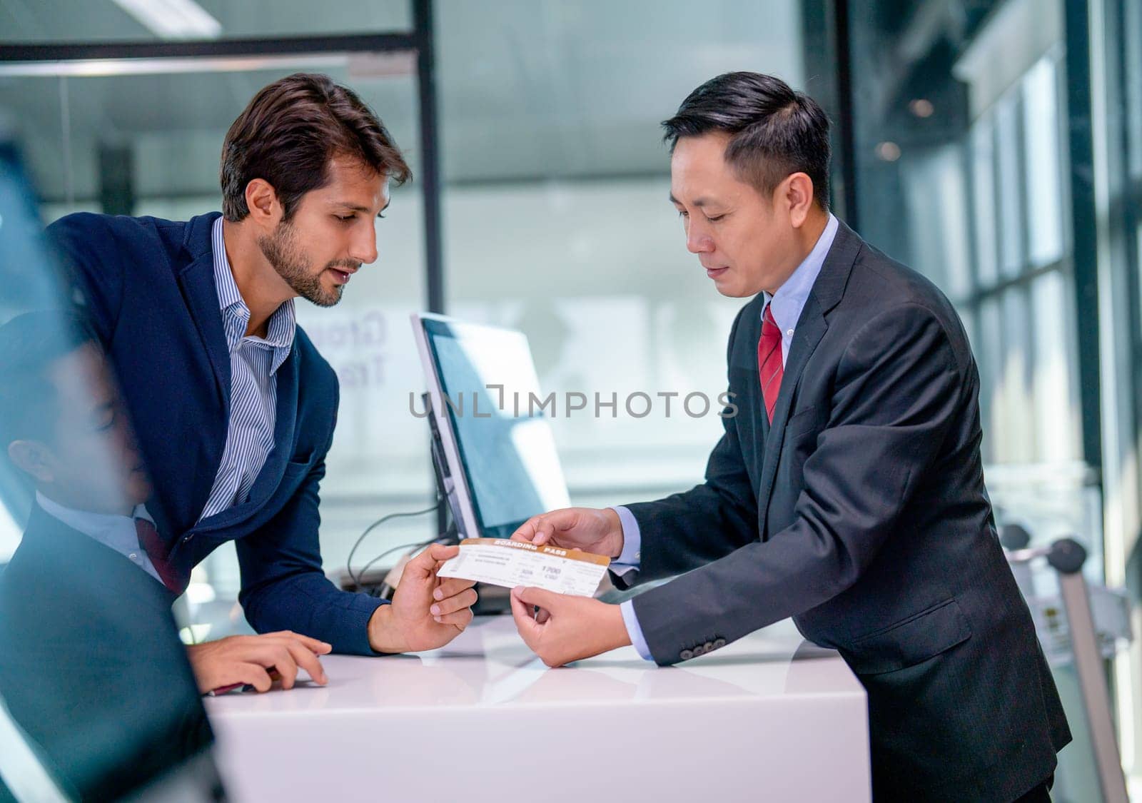 Airline staff give boarding pass to the passenger business man and explain about the detail at counter service in the airport.