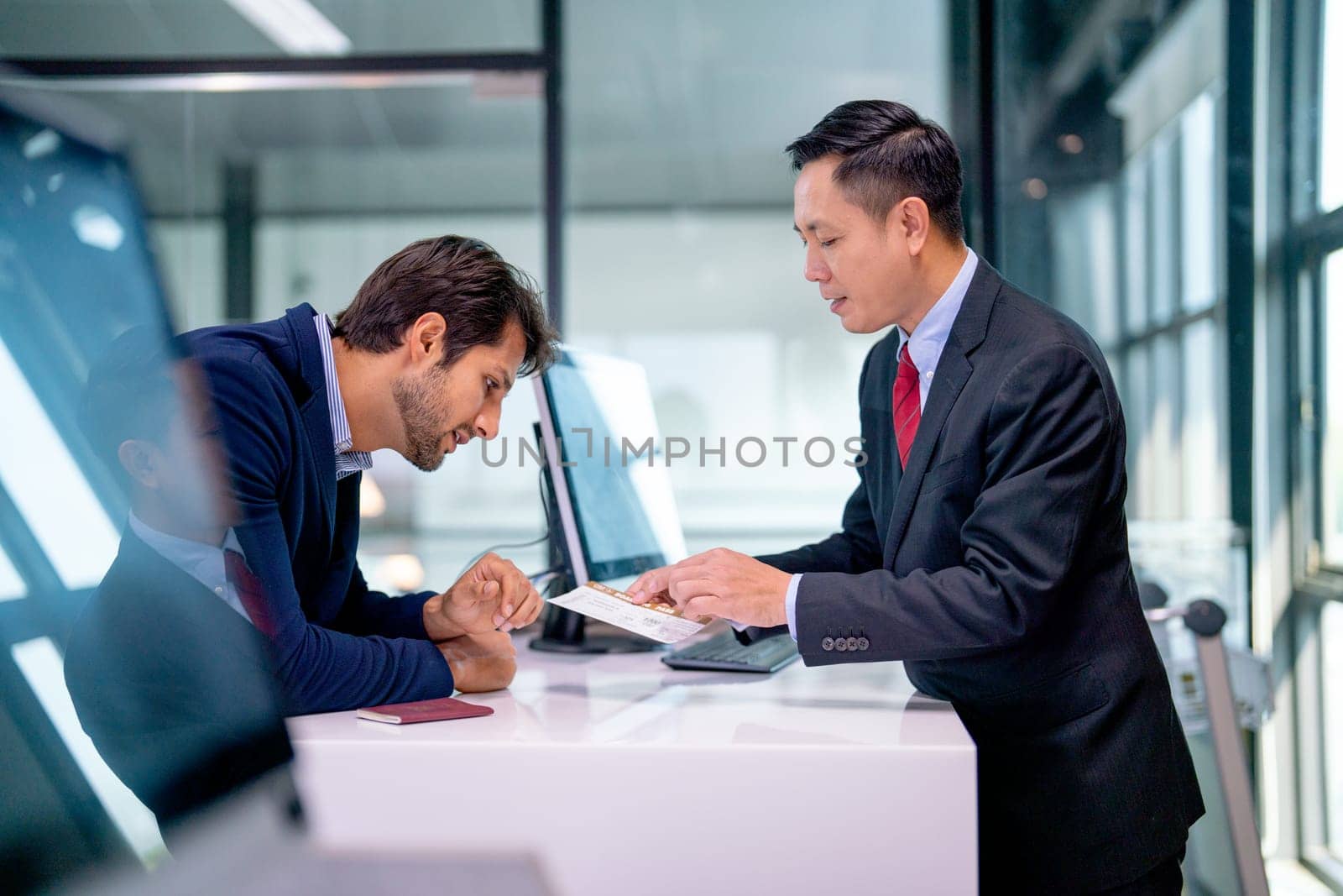 Airline staff give boarding pass to the passenger business man and explain about the detail at counter service in the airport.