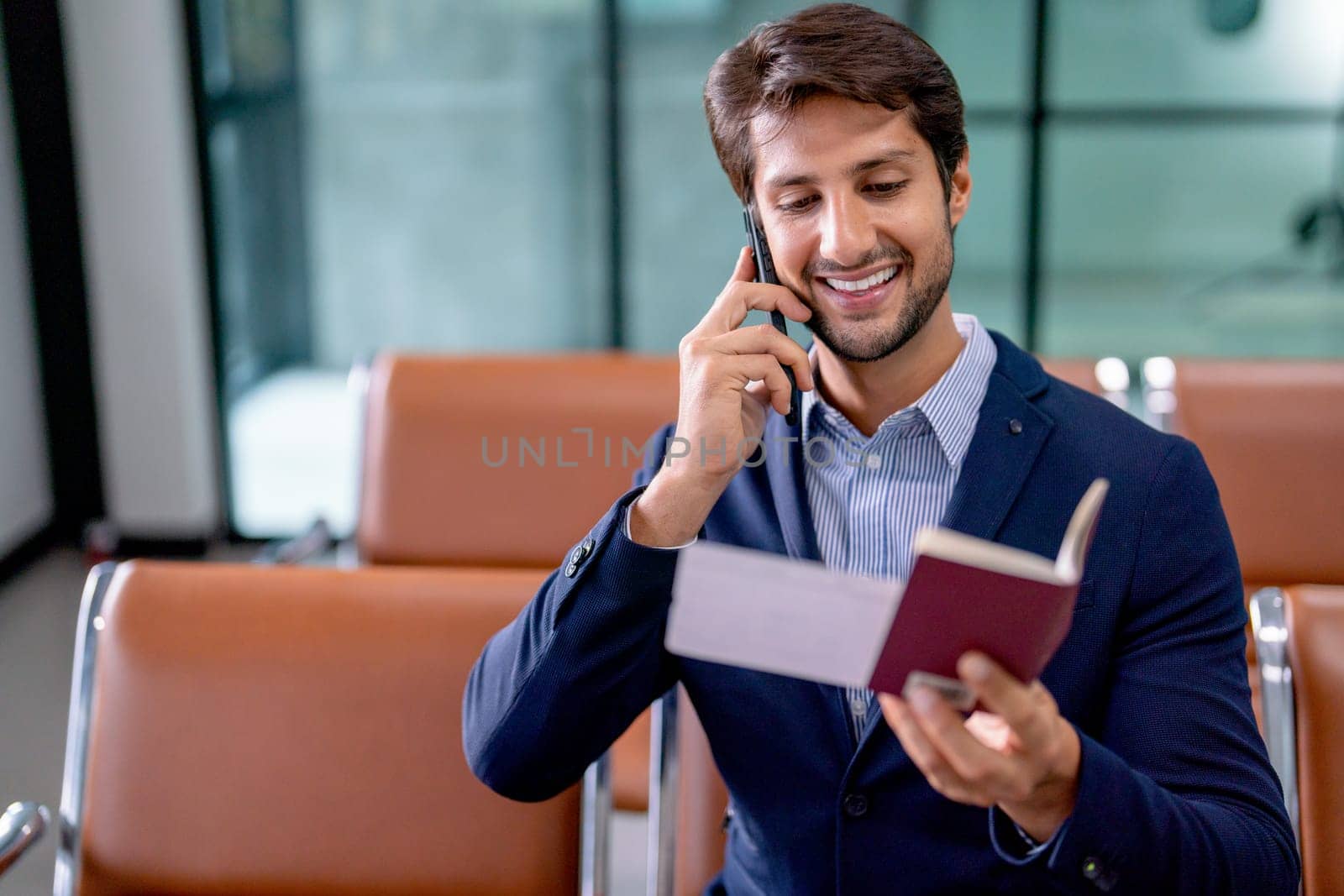 Portrait of business man hold passport and boarding pass also use mobile phone to contact with his friend during wait to the flight go to the other city.