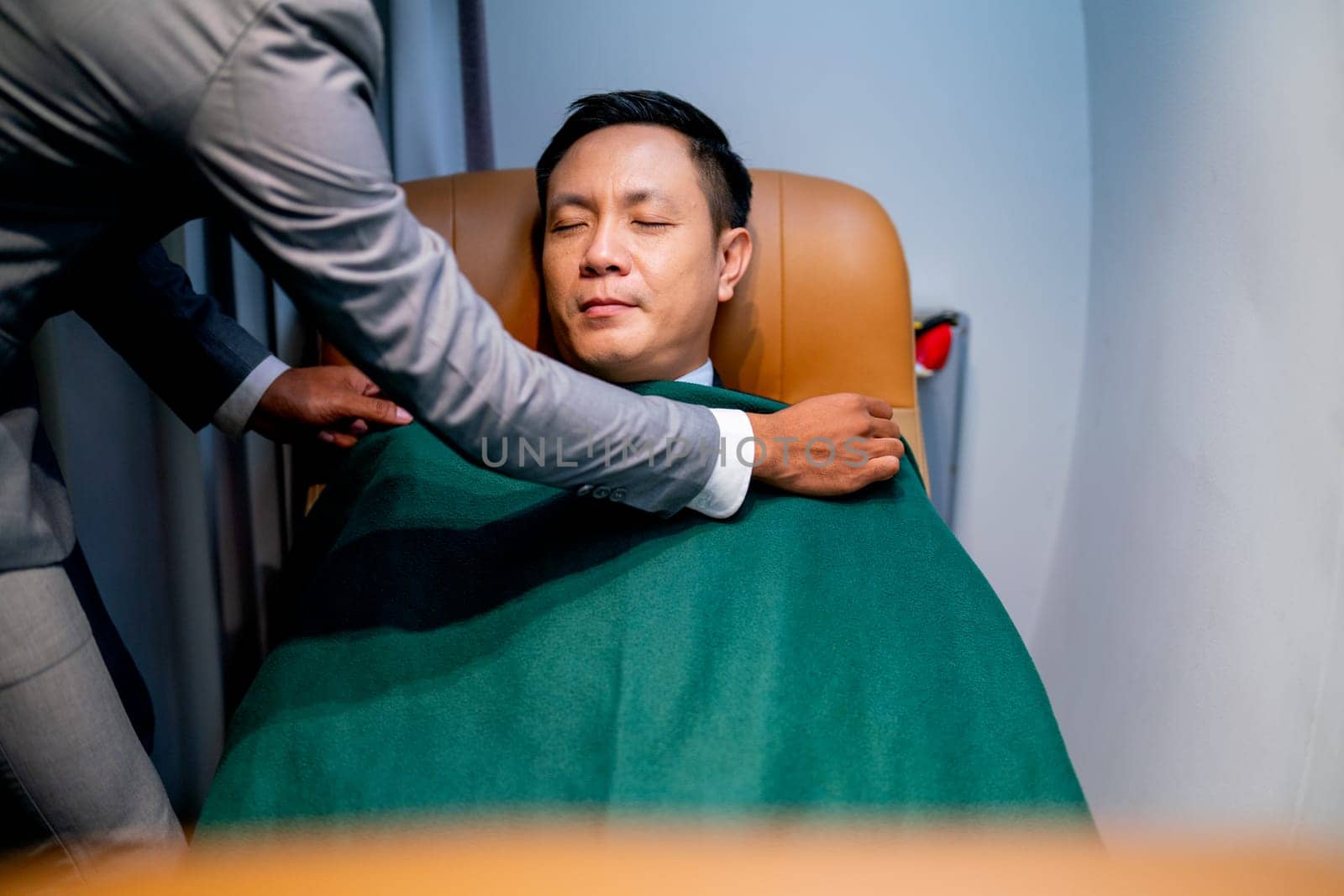 Airline staff help to cover the blanket to customer business man during flight for working.