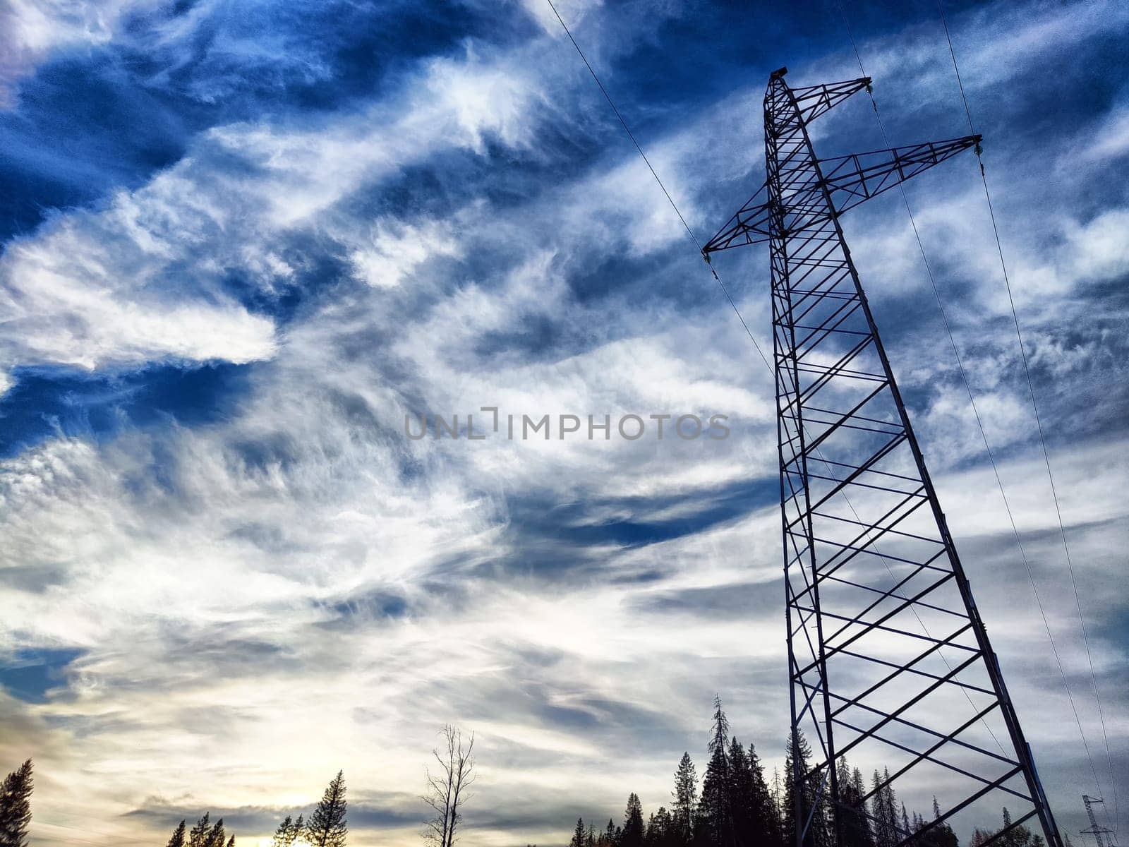 Power lines on a hill, hill or in the mountains against a blue sky with white clouds. Electric lines, towers, wires in nature landscape