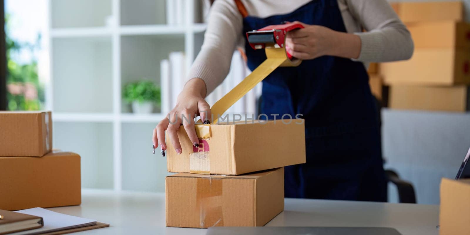 Woman use scotch tape to attach parcel box to prepare goods for the process of packaging, shipping, online sale internet marketing ecommerce concept startup business idea.