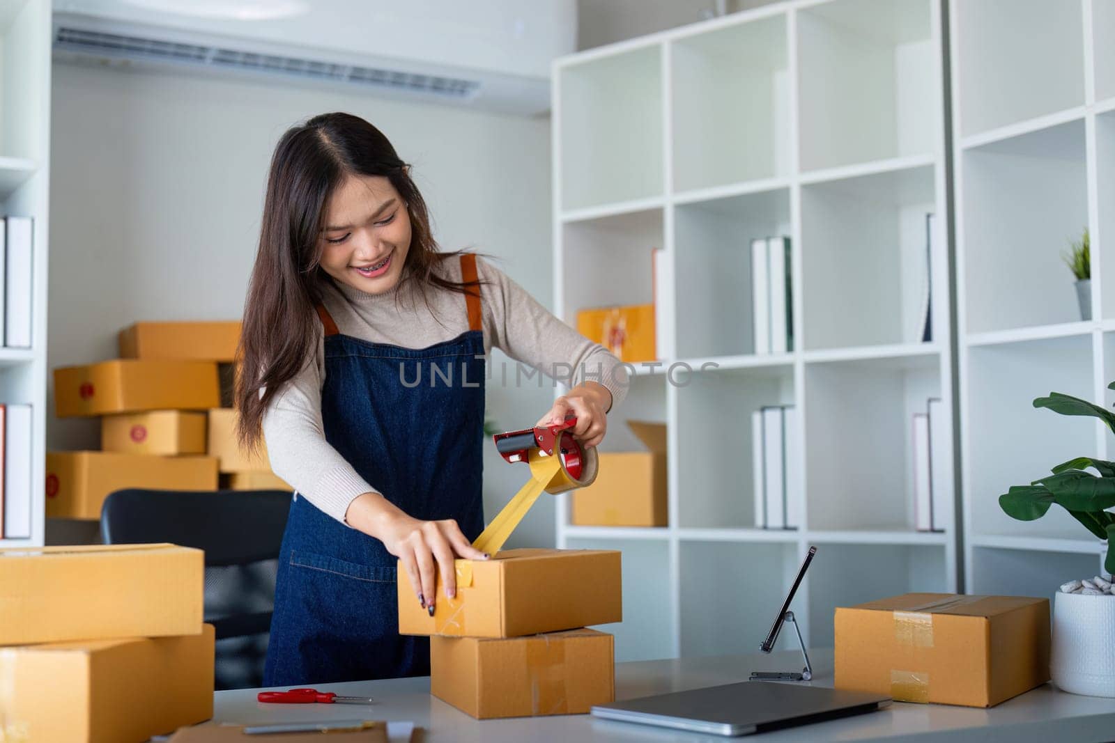 Woman use scotch tape to attach parcel box to prepare goods for the process of packaging, shipping, online sale internet marketing ecommerce concept startup business idea by nateemee