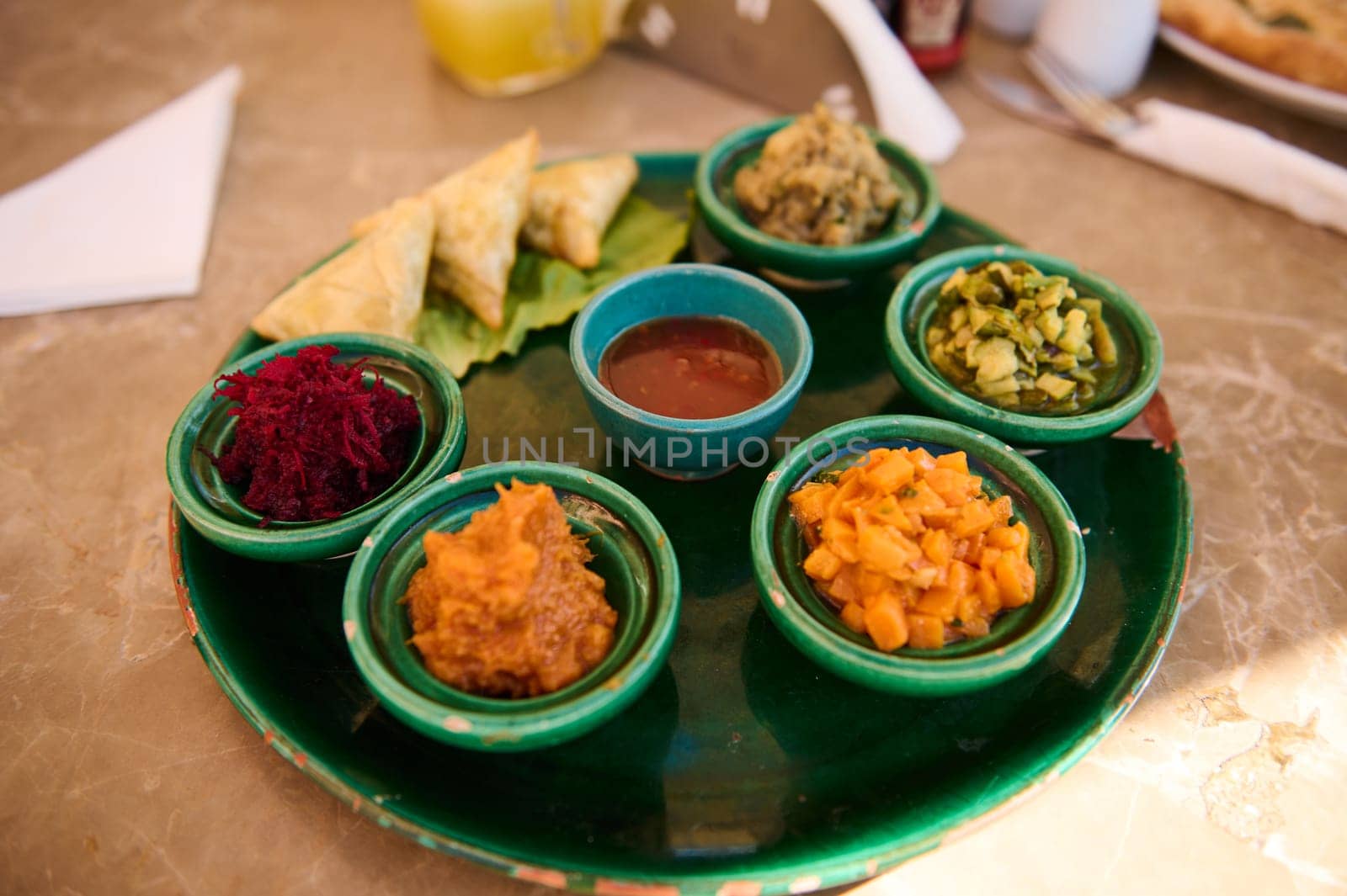 View from above of a table in restaurant with served plate of Moroccan traditional dish, vegetarian salads and sauces served in small ceramic tagines. Travel, food background, restaurant business