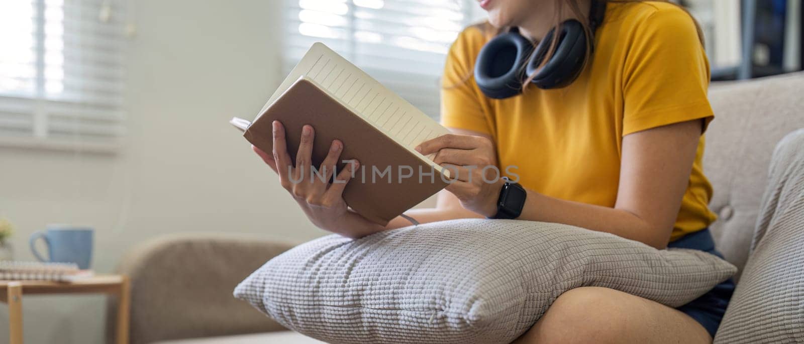 Young woman siting on sofa and reading a book enjoys of rest. relaxing at home by nateemee