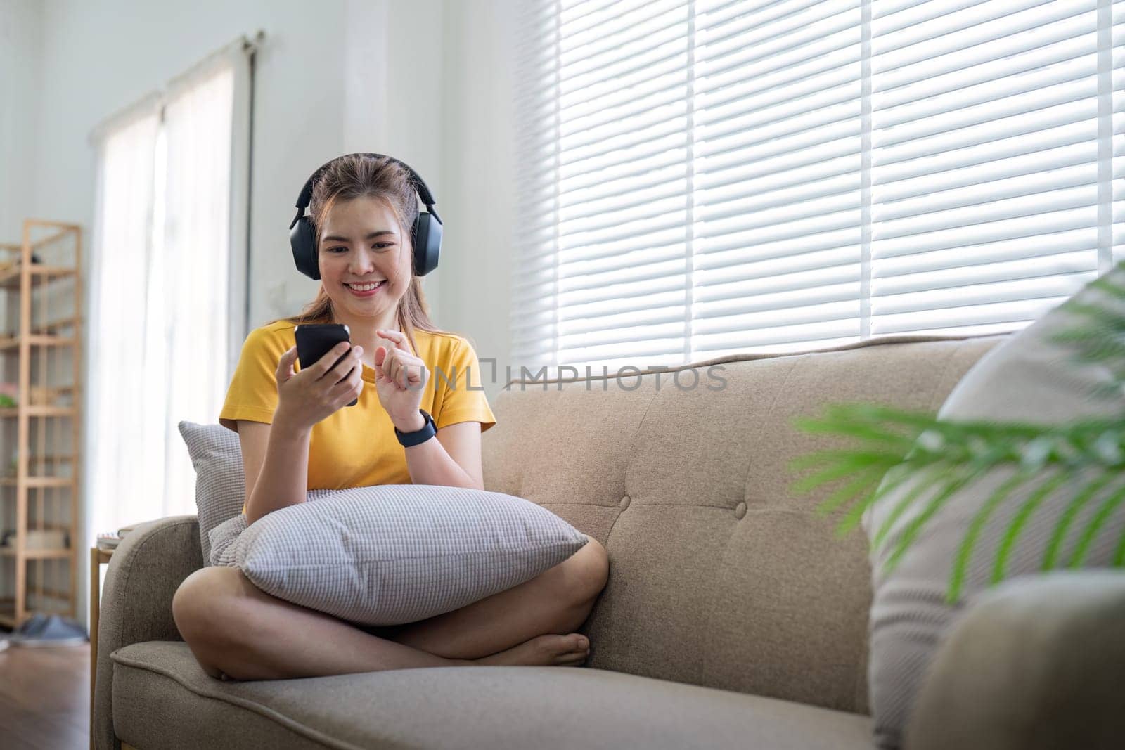 Young asian woman using mobile phone and earphones to listening to music or online chatting at home by nateemee