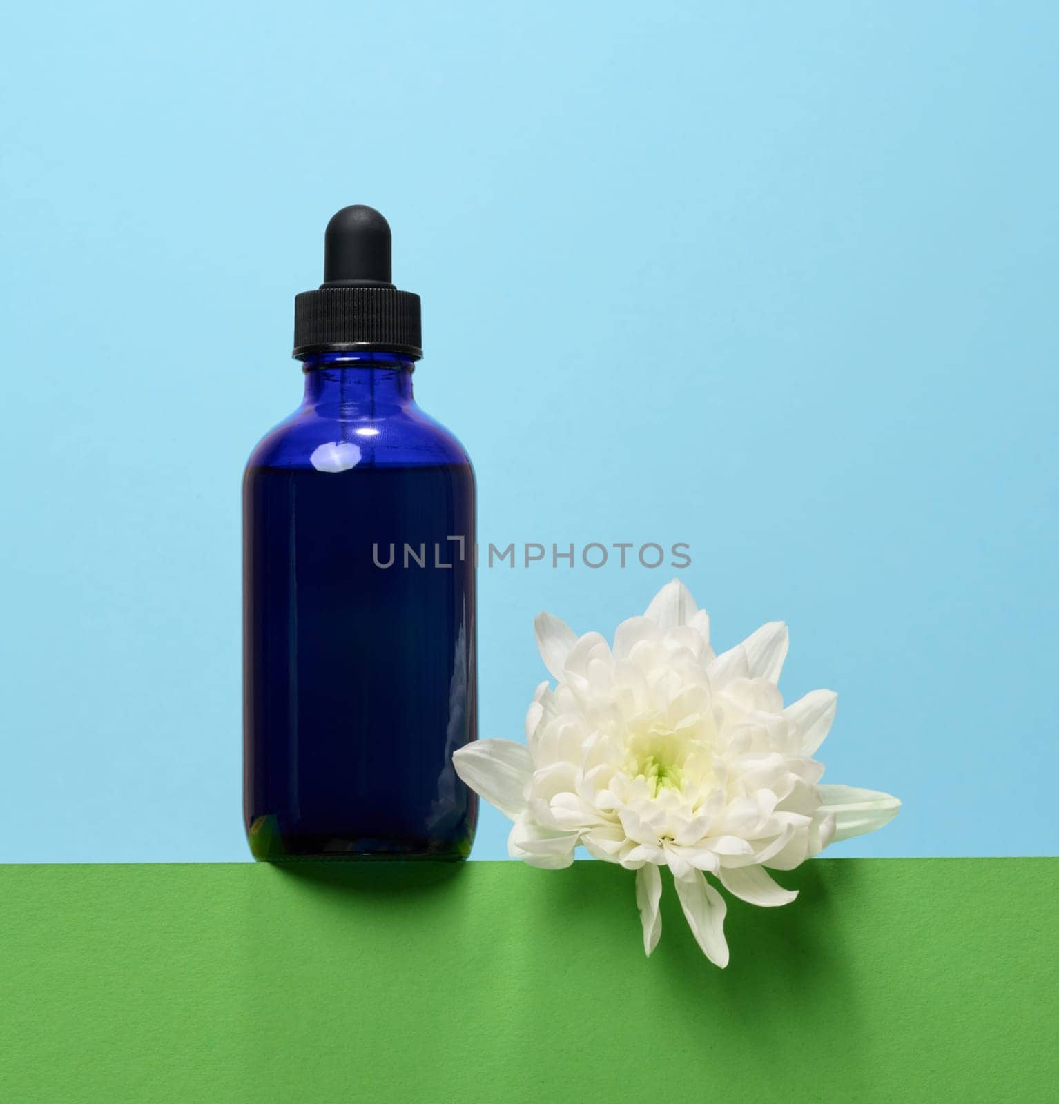 A glass blue bottle with a dropper on a blue background, a container for cosmetic products.  by ndanko