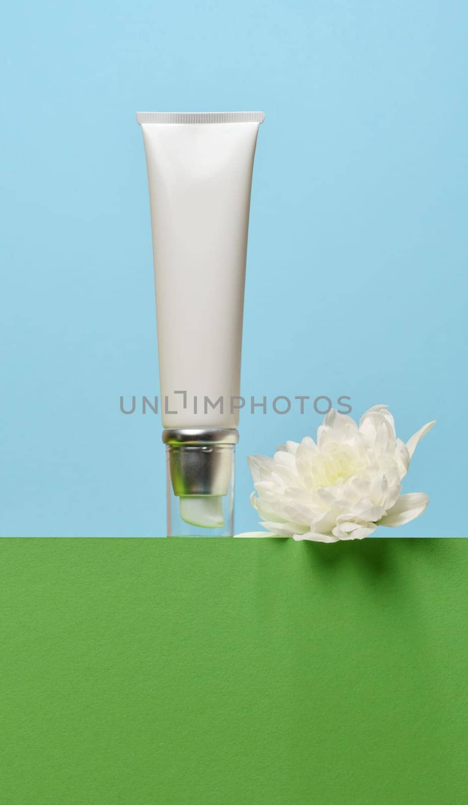 White plastic tube with a transparent cap and dispenser on an green background, container for cosmetics