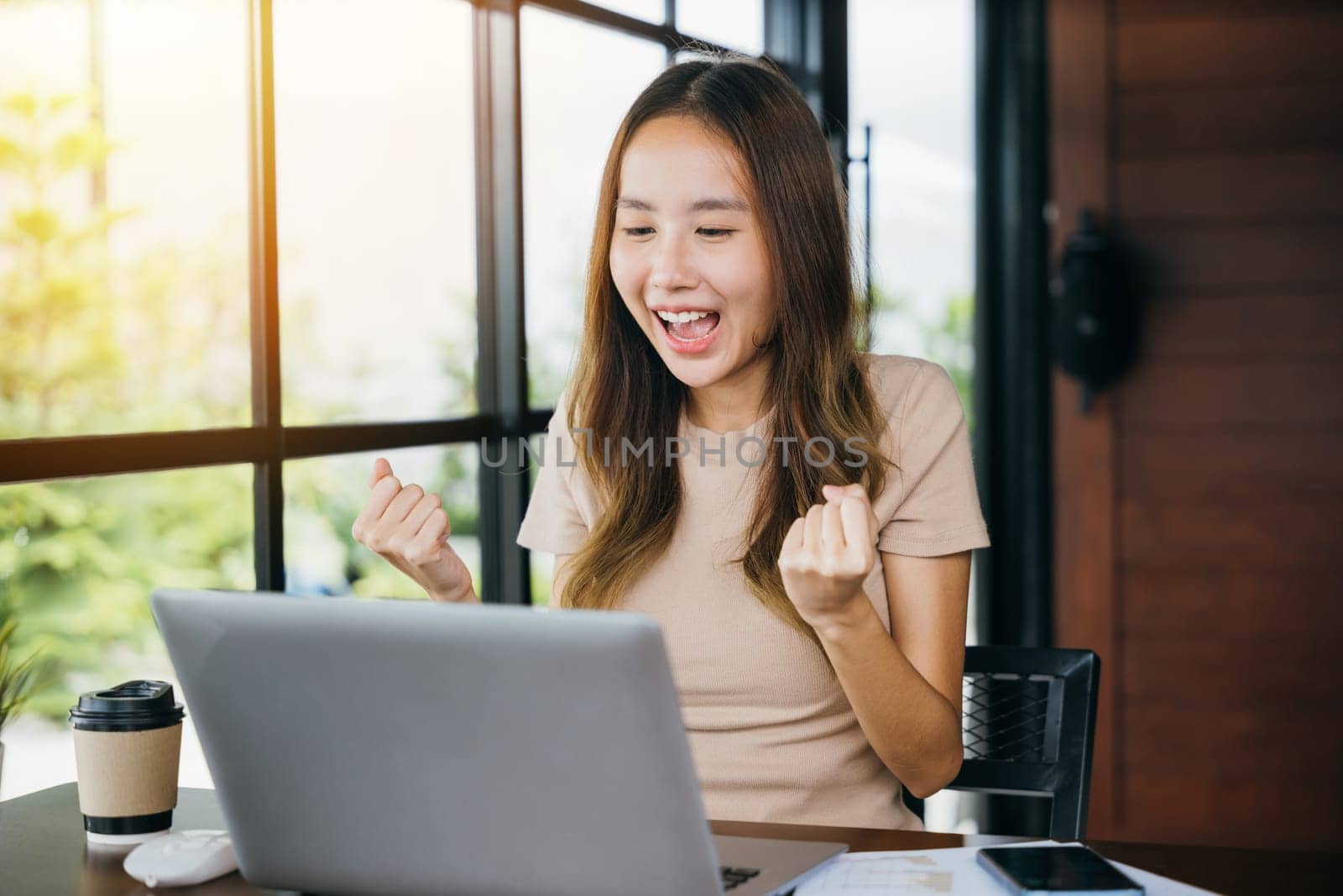 Excited female feeling winner rejoicing online win got new job on laptop computer at home, happy Asian business young woman sitting at cafe desk raising hands up and celebrating success