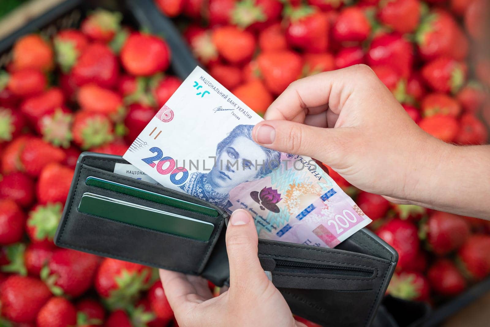 Girl buying strawberry at the market and taking 200 hryvnias from the purse by VitaliiPetrushenko