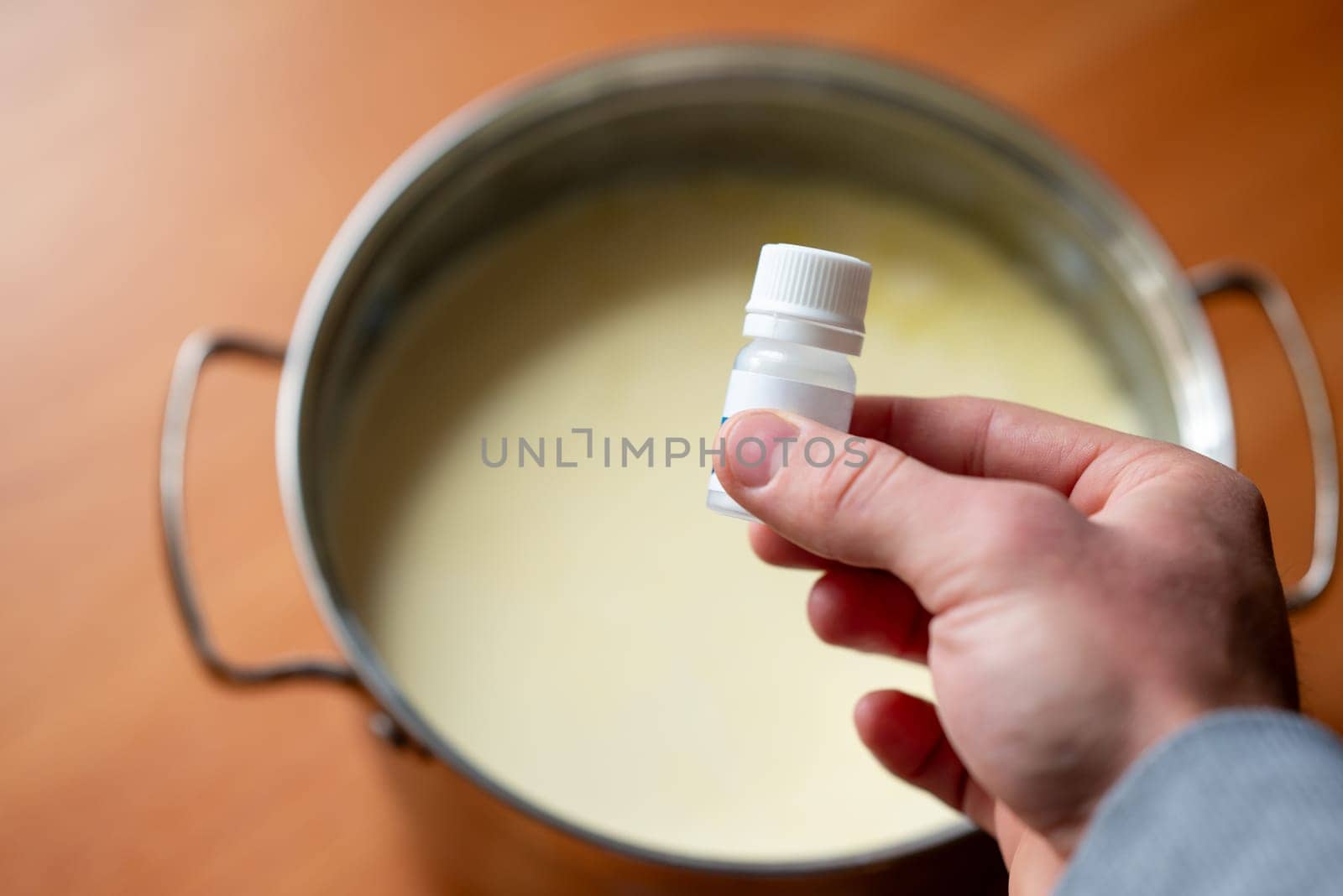 Male hand holding ferment for making yogurt above the pot with milk, close up by VitaliiPetrushenko