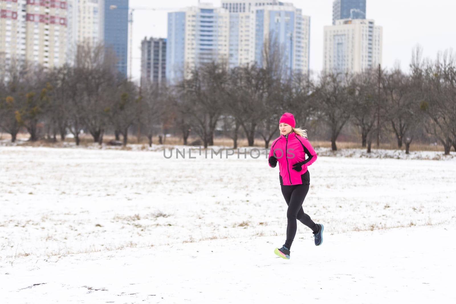 Winter running in park: happy woman runner jogging in snow, outdoor sport and fitness concept . High quality photo