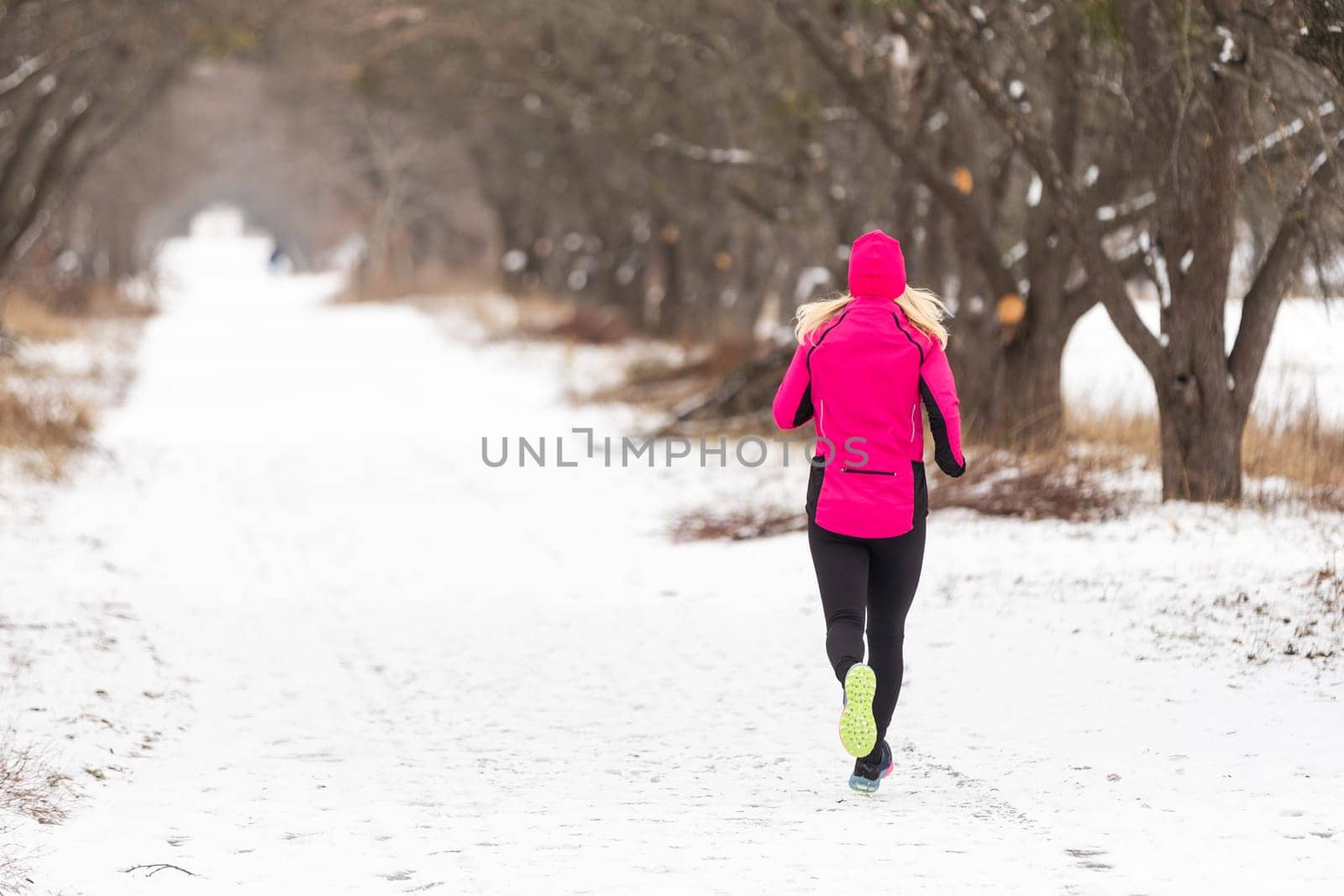 Winter running in park: happy woman runner jogging in snow, outdoor sport and fitness concept by Andelov13