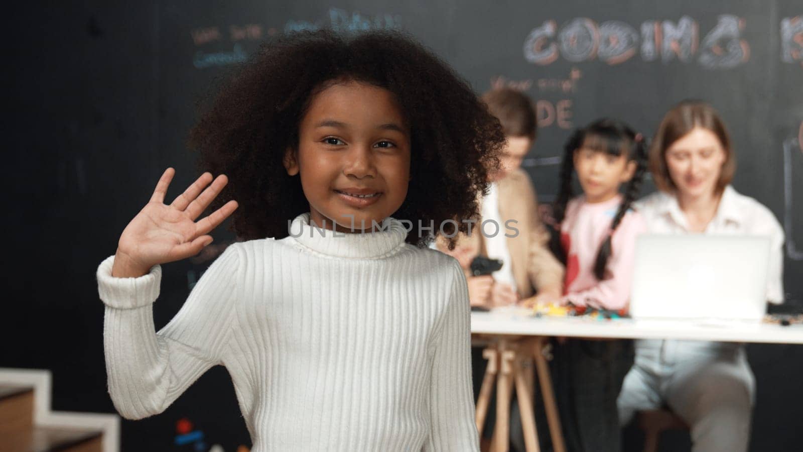 African girl smiling and looking at camera while multicultural friends working or learning engineering code or prompt in STEM technology classroom from young beautiful caucasian teacher. Erudition.