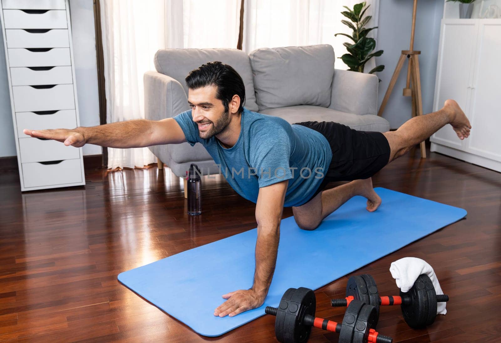 Flexible and dexterity man in sportswear doing yoga position in meditation posture on exercising mat at home. Healthy gaiety home yoga lifestyle with peaceful mind and serenity.