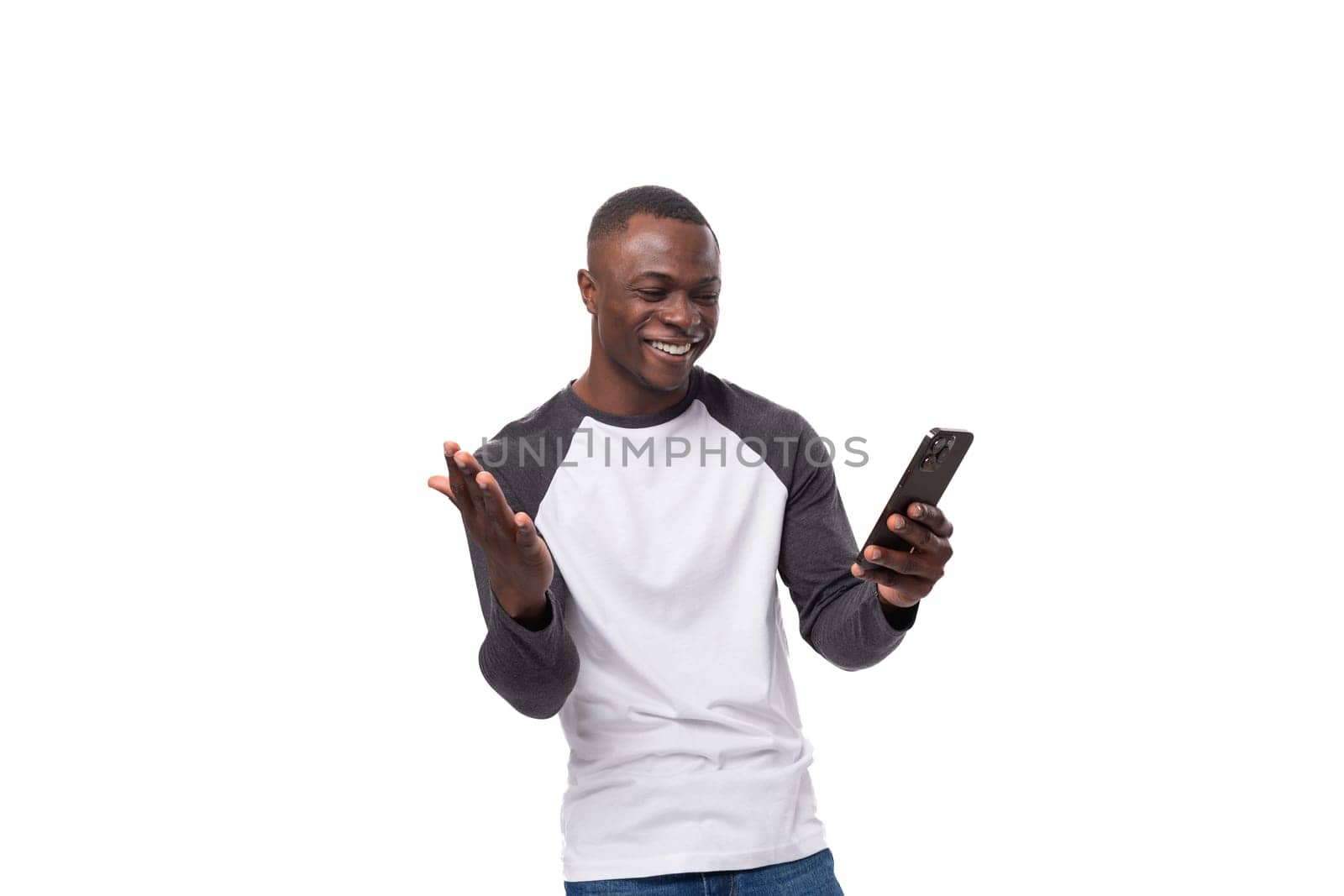 a young african guy with a short haircut dressed in a summer long-sleeve sweater uses online transfer using a smartphone.