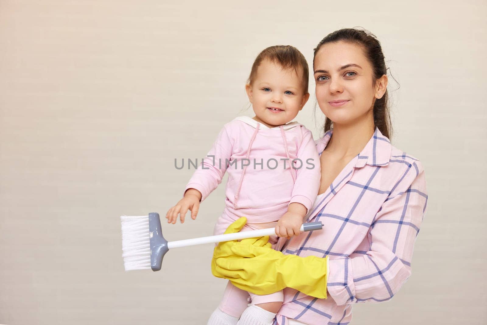 smiling mother housewife is holding cute baby girl and doing housework at home, Happy family, copy space