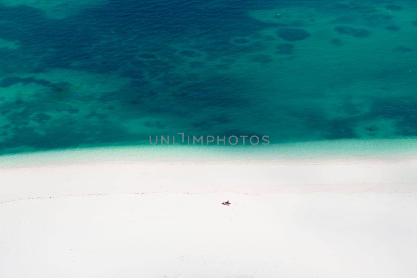 Drone view of white sandy beach in the green ocean and one tourist alone, minimalist photo and copy space, summer concept, Zanzibar in Tanzania.