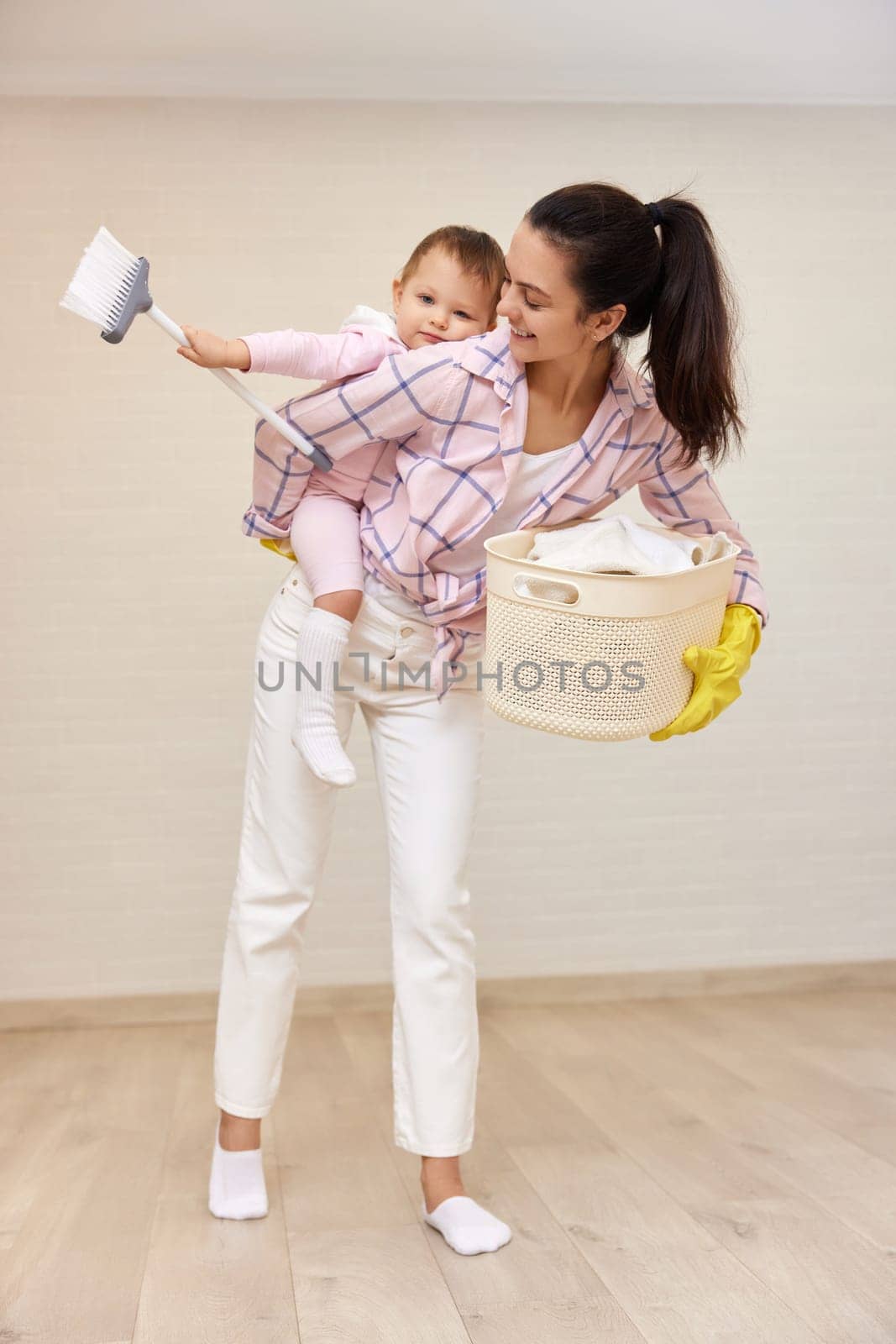 happy mother housewife is holding cute baby girl and basket with laundry at home, Happy family