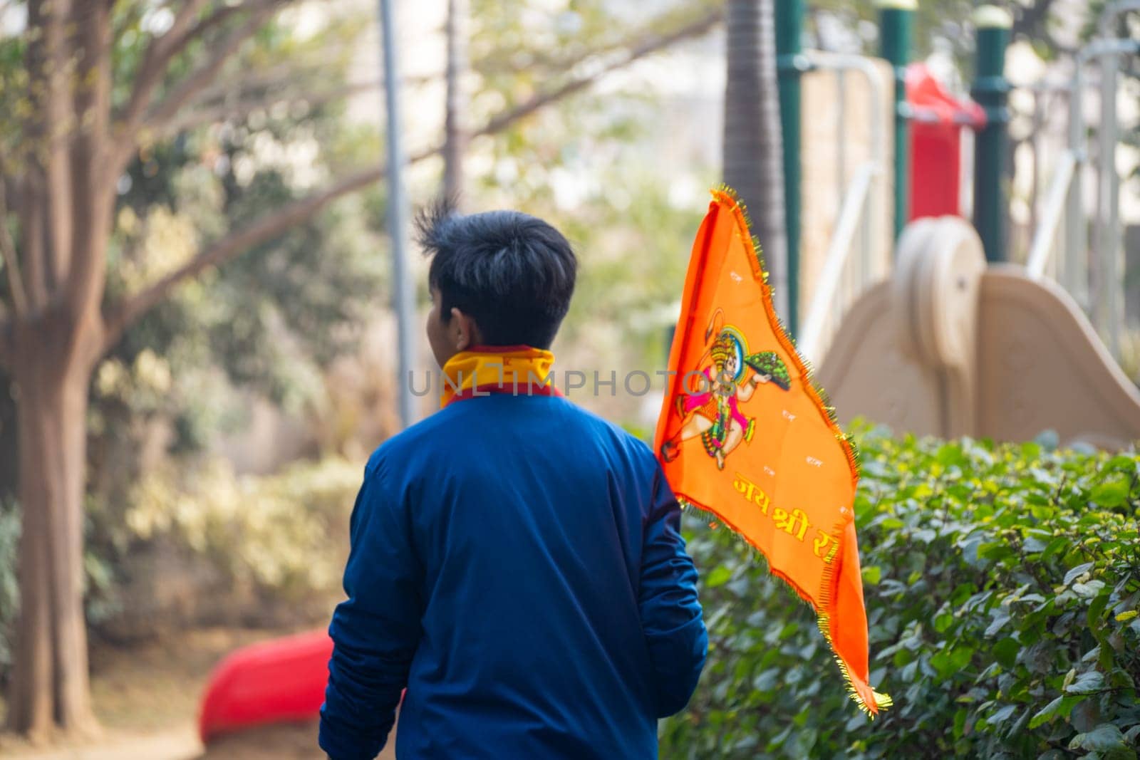 Ayodhya, Uttar Pradesh, India - 22nd Jan 2024: Young man walking carrying flag celebrating the Pran Pratishtha consecration of Ram mandir temple massive celebration in India in park