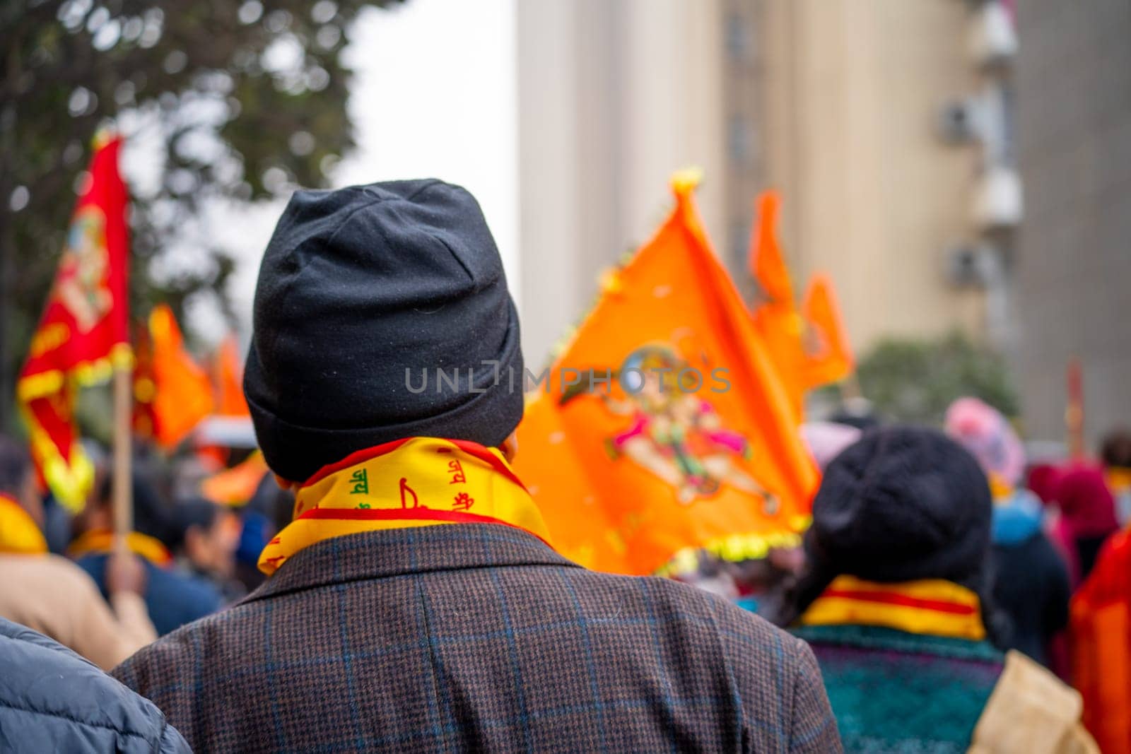 Focus blur shot showing back of old man wearing winter clothes and bhagwa saffron scarf walking with crowd carrying flag celebrating the Pran Pratishtha consecration of Ram mandir temple by Shalinimathur