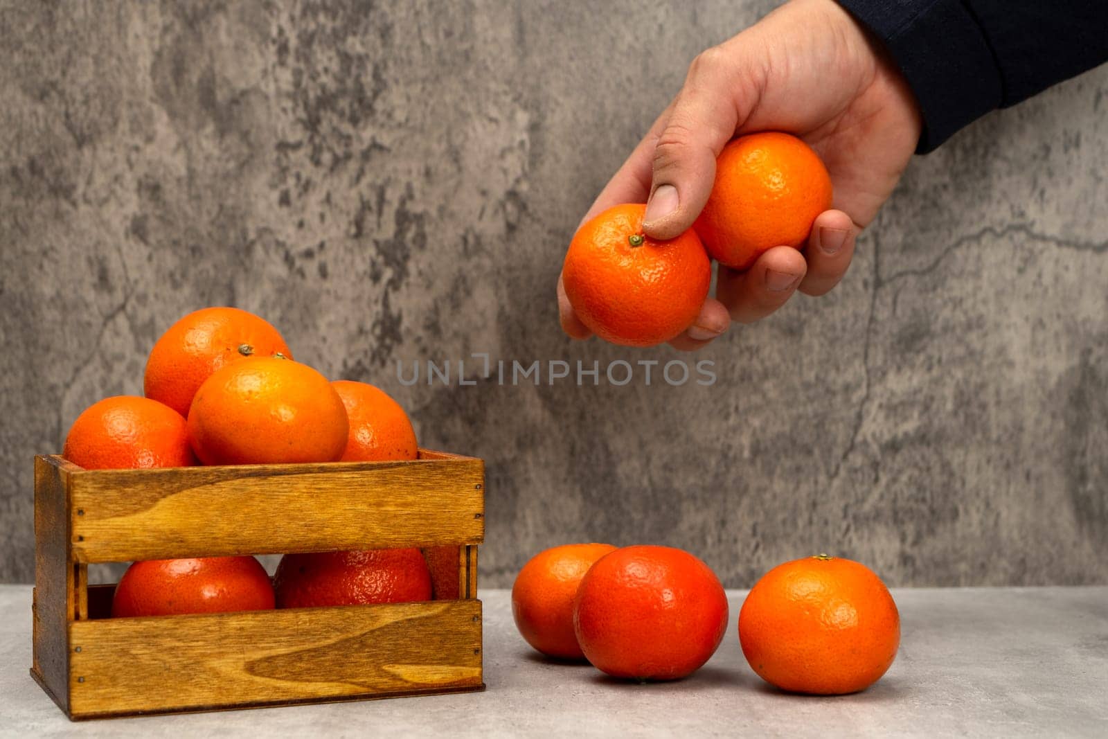 Man's hand picking some ripe oranges in a still life with gray background, healthy living concept. Superfood rich in vitamin C