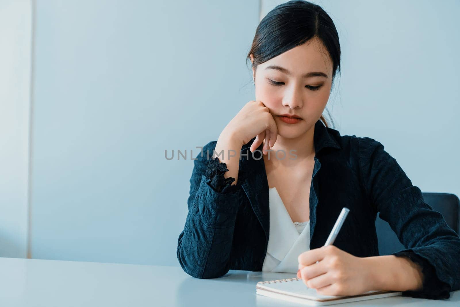 Beautiful young Asian woman writes letter on notebook while sitting at office desk. Content writer and secretary job concept. uds