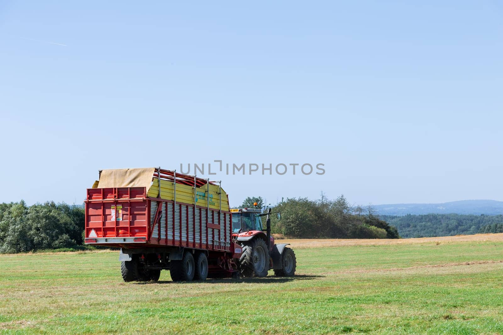 Hay tractor with trailer is working in field. Modern hay harvesting equipment.