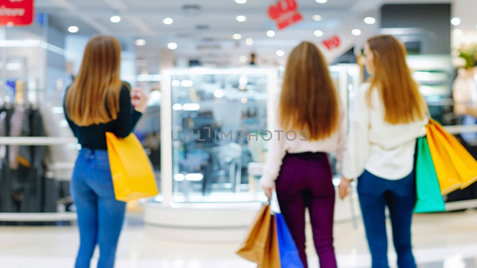 sale, consumerism and people concept - blurred happy young women with shopping bags walking in mall by Costin