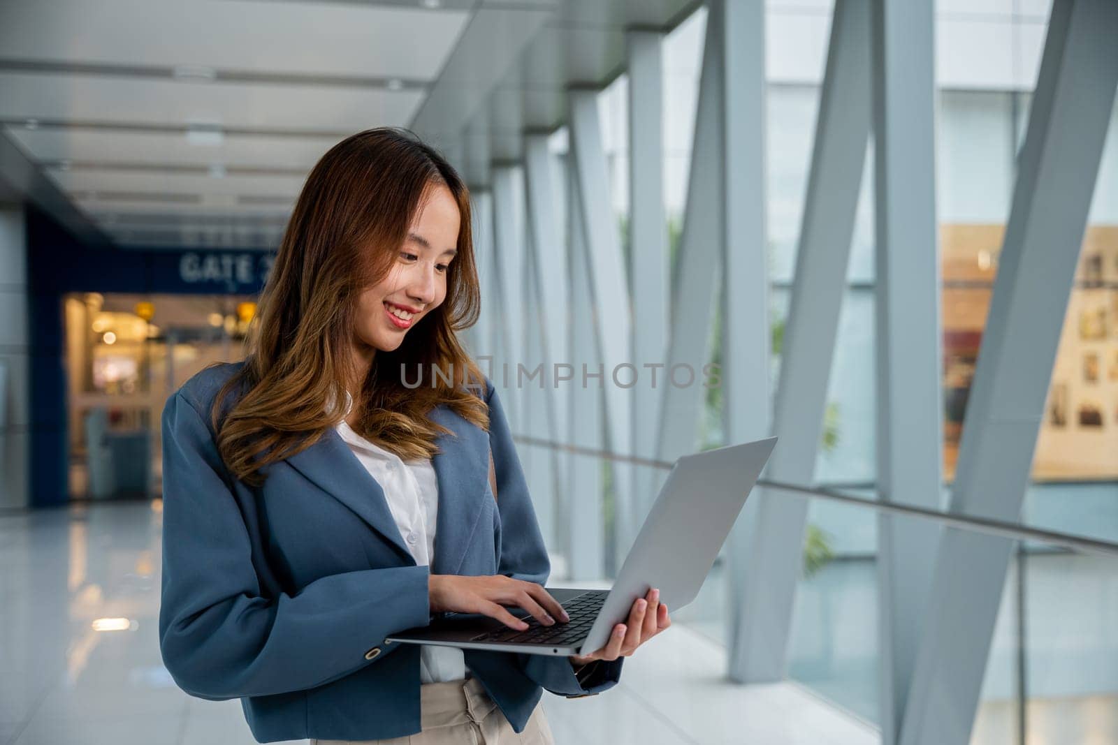 Portrait of young adult woman working on laptop and talking on cellphone in airport by Sorapop