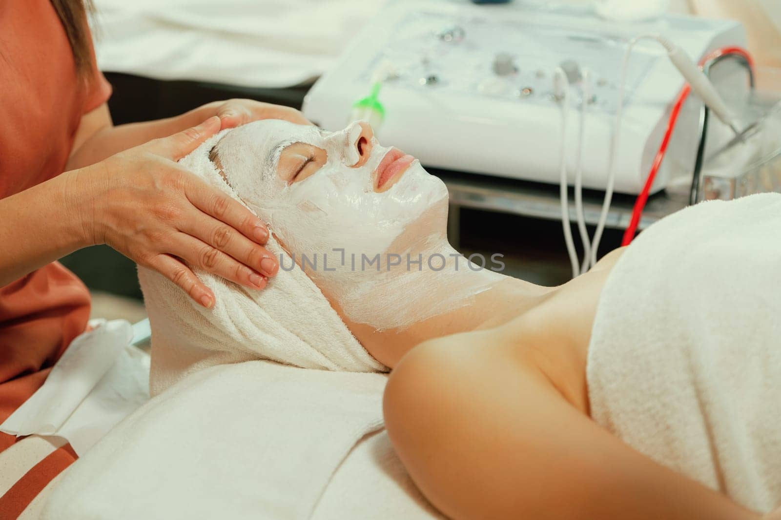 Beautiful young women lie on spa bed while having facial massage from professional doctor. Attractive female with beautiful skin surrounded by electric facial machine. Tranquility.